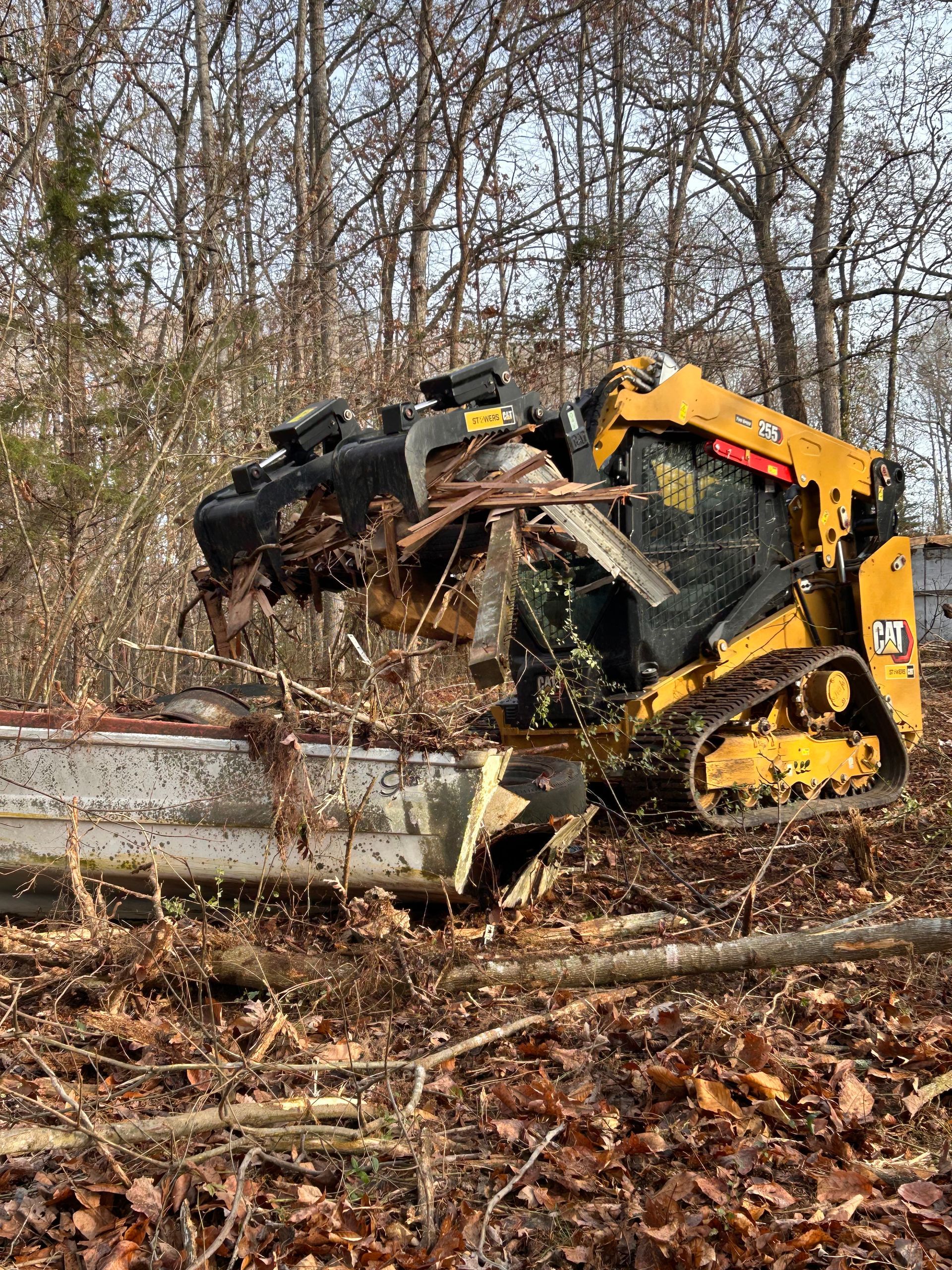 Yellow skid steer with forestry cutter clearing branches and debris in a wooded area.
