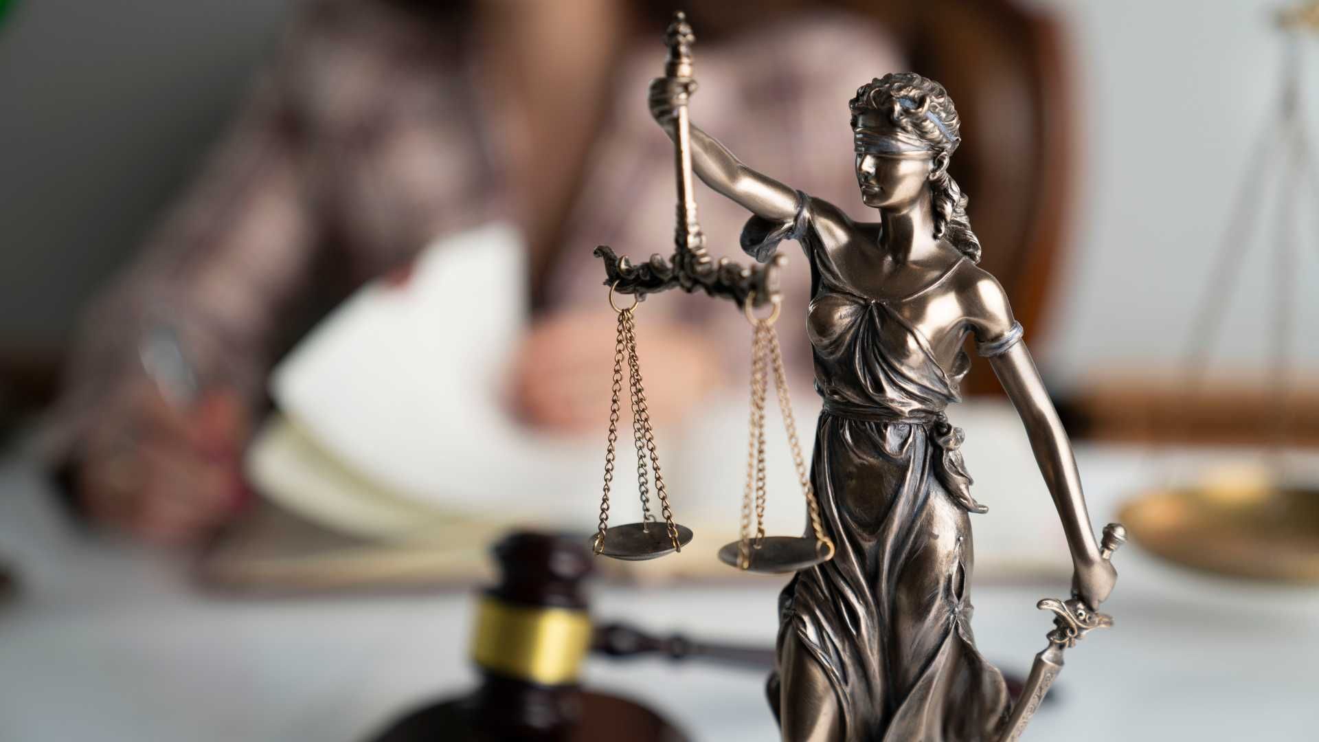 A statue of lady justice is sitting on a table next to a gavel.