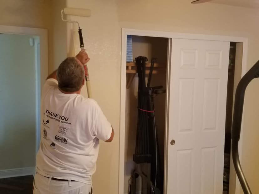 A man in a white shirt is painting a wall with a roller.