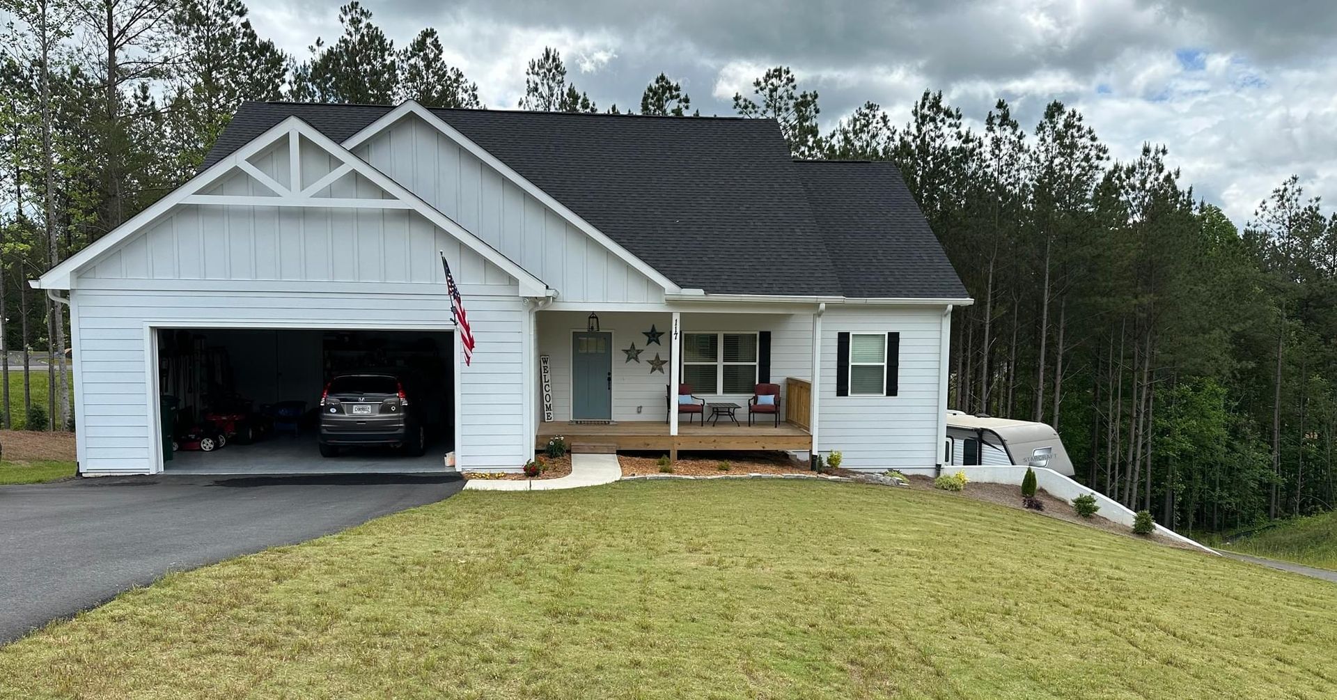A white house with a black roof and a car parked in the garage.