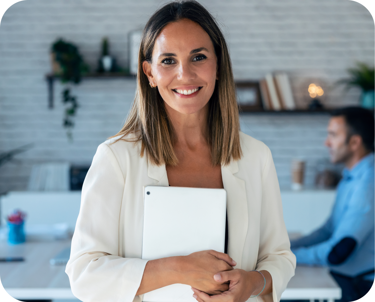 A woman is holding a tablet and smiling in an office.
