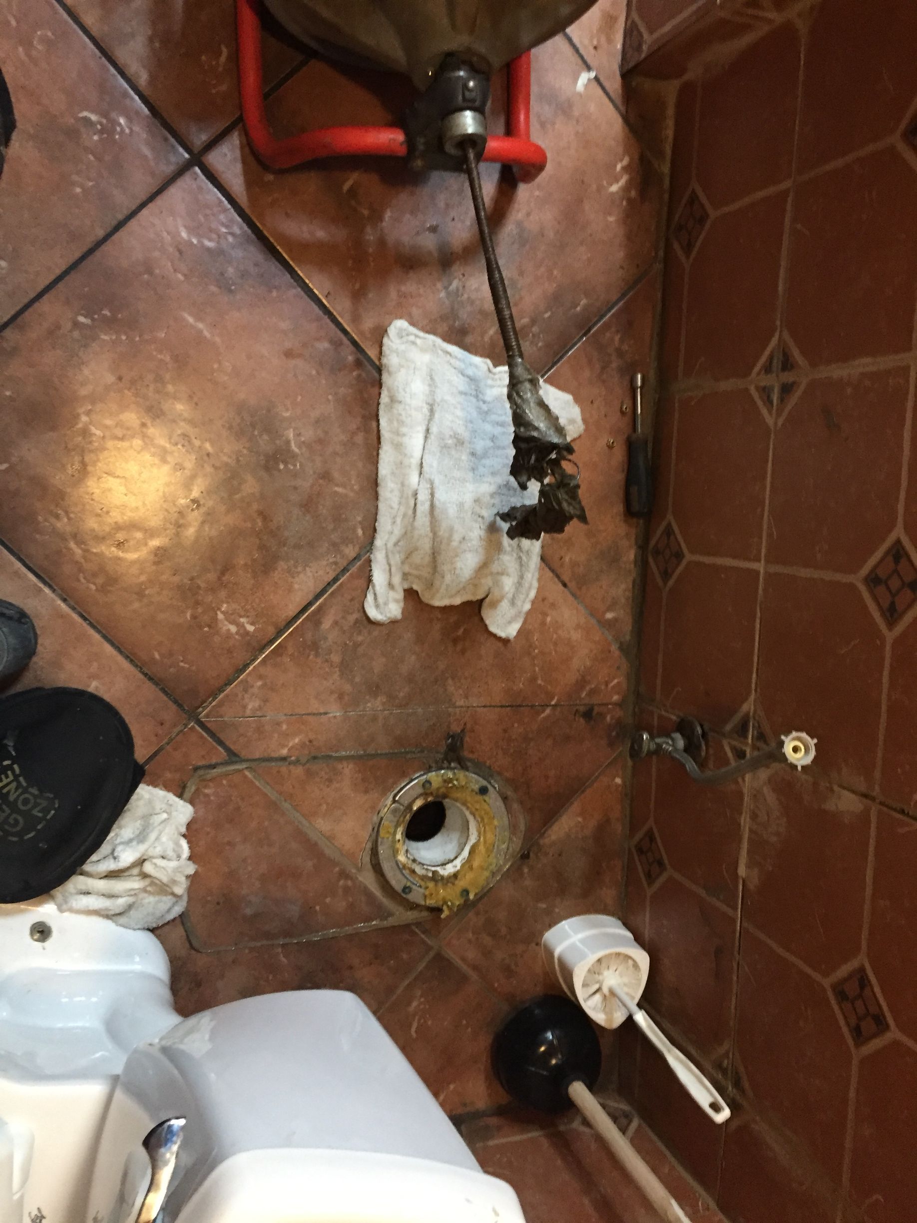 A toilet with a toilet brush and a towel on the floor.