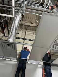 Two men are working on the ceiling of a building.