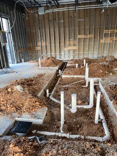 A room under construction with a lot of pipes in the dirt.