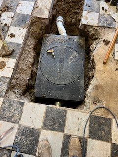 A man is standing in a hole in the floor next to a pipe.