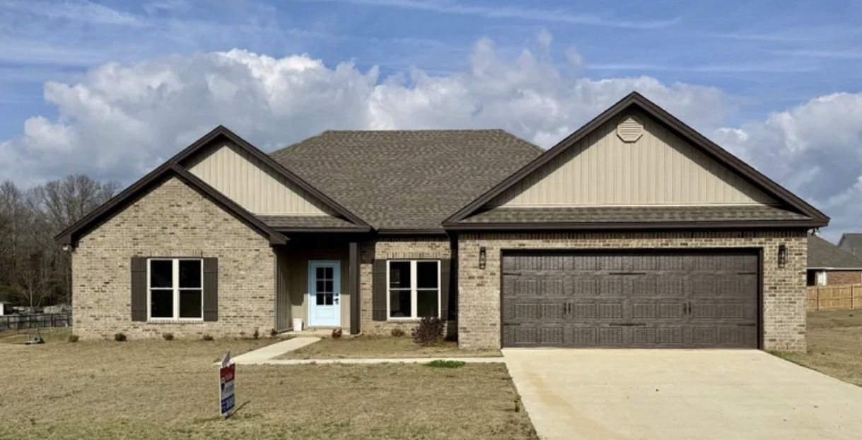 Single-story brick house with gabled roof, two-car garage, and driveway under a partly cloudy sky