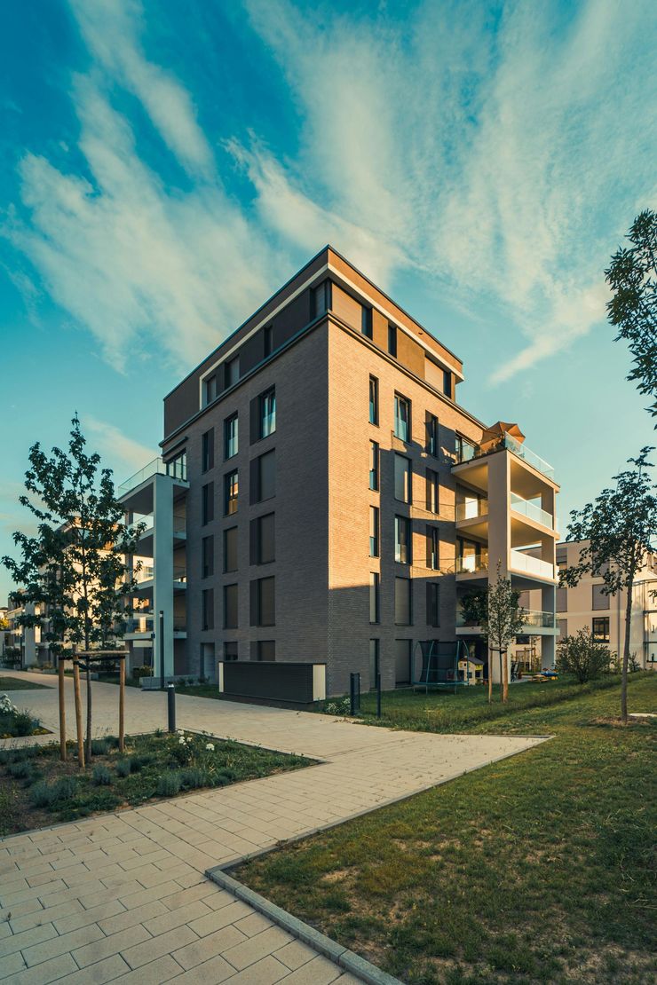 Modern apartment building with balconies beside a paved path and trees at sunset
