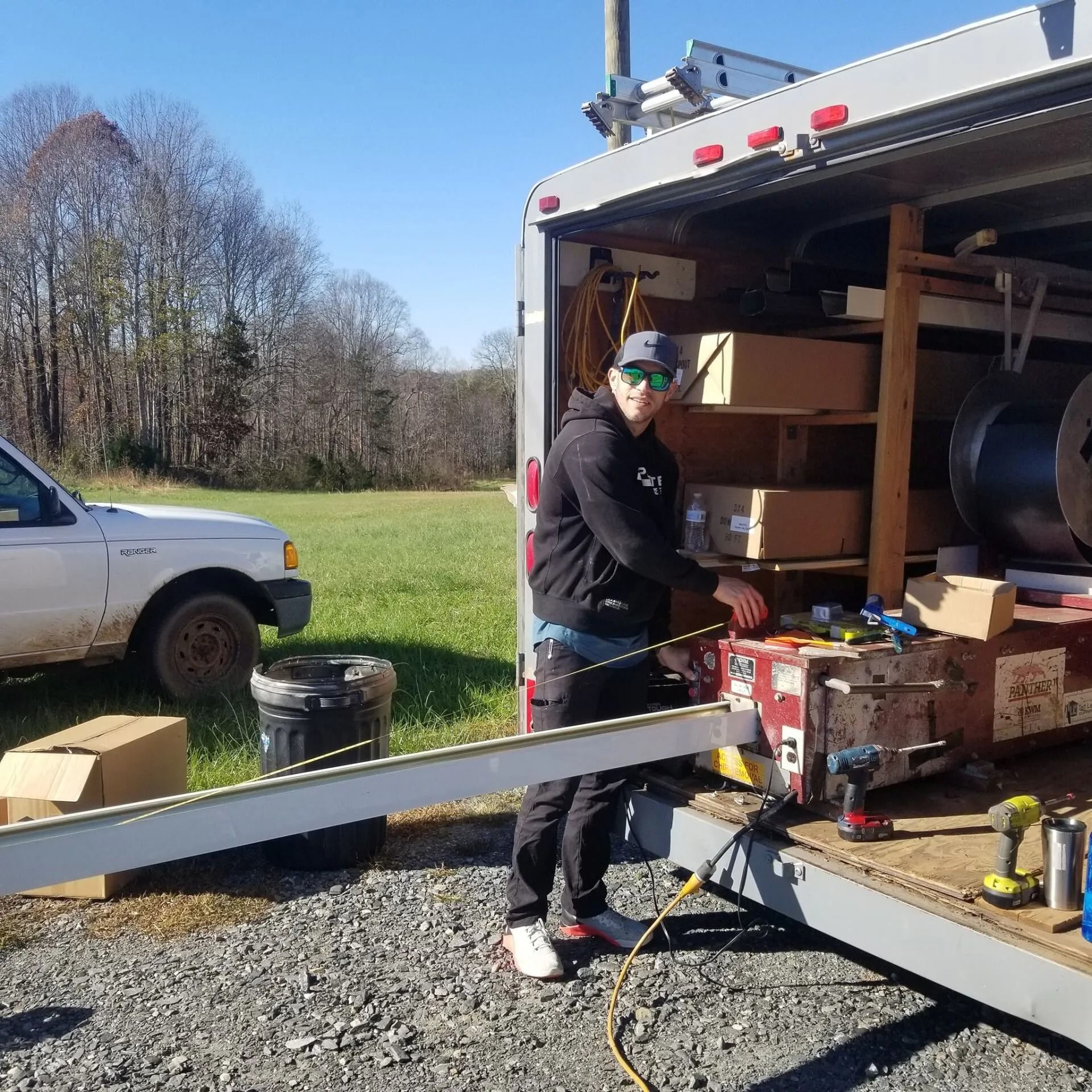 Man working by open cargo truck with tools and supplies. Outdoors, sunny day.