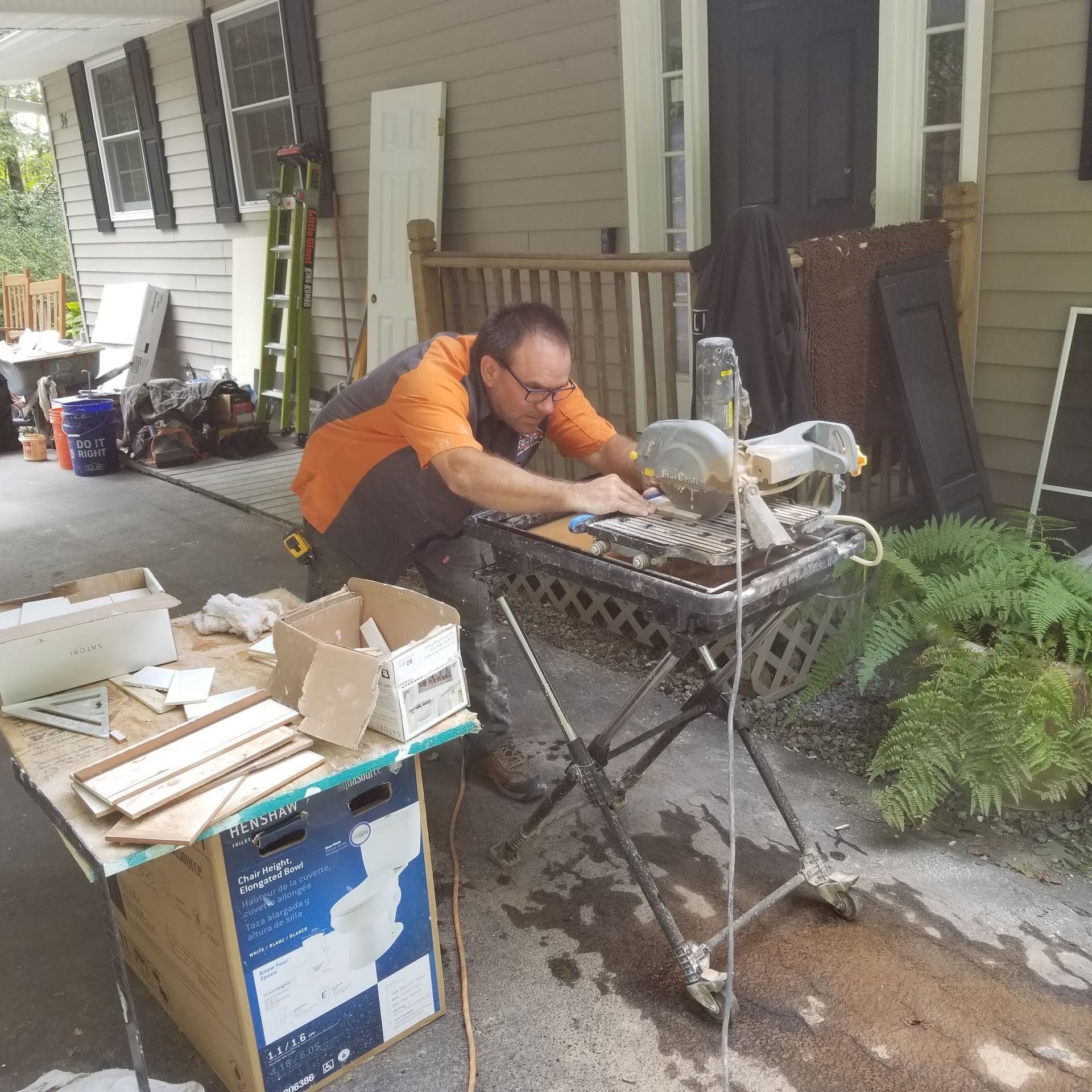 Man using a tile saw outdoors on a porch. He is cutting tile with a table saw on a stand.