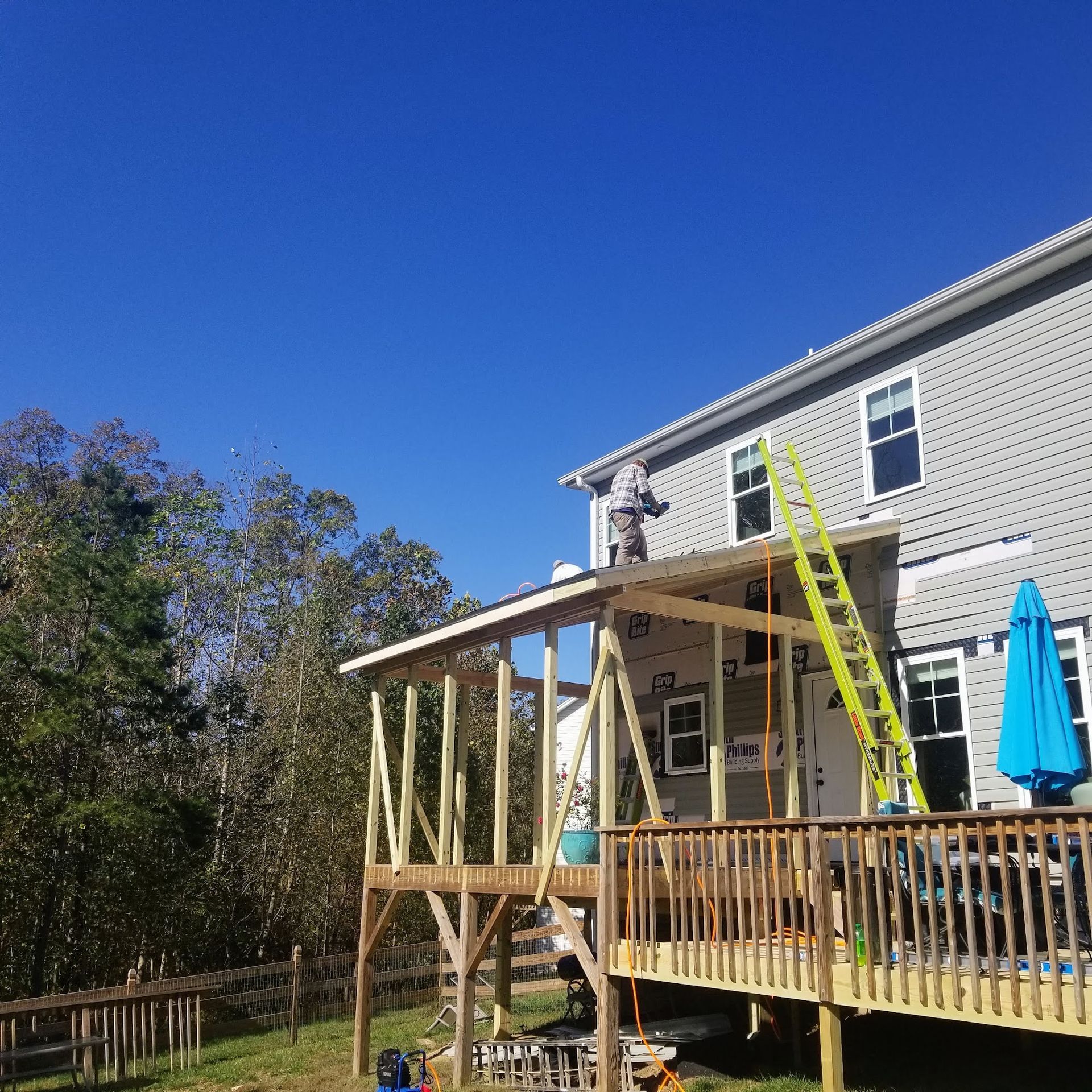 Construction worker on a roof adding a covered deck to a house on a sunny day.