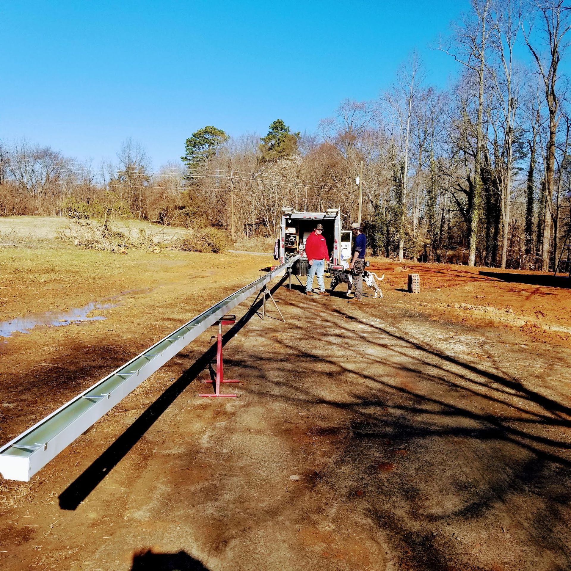 Men installing a long metal gutter system outdoors on a sunny day.
