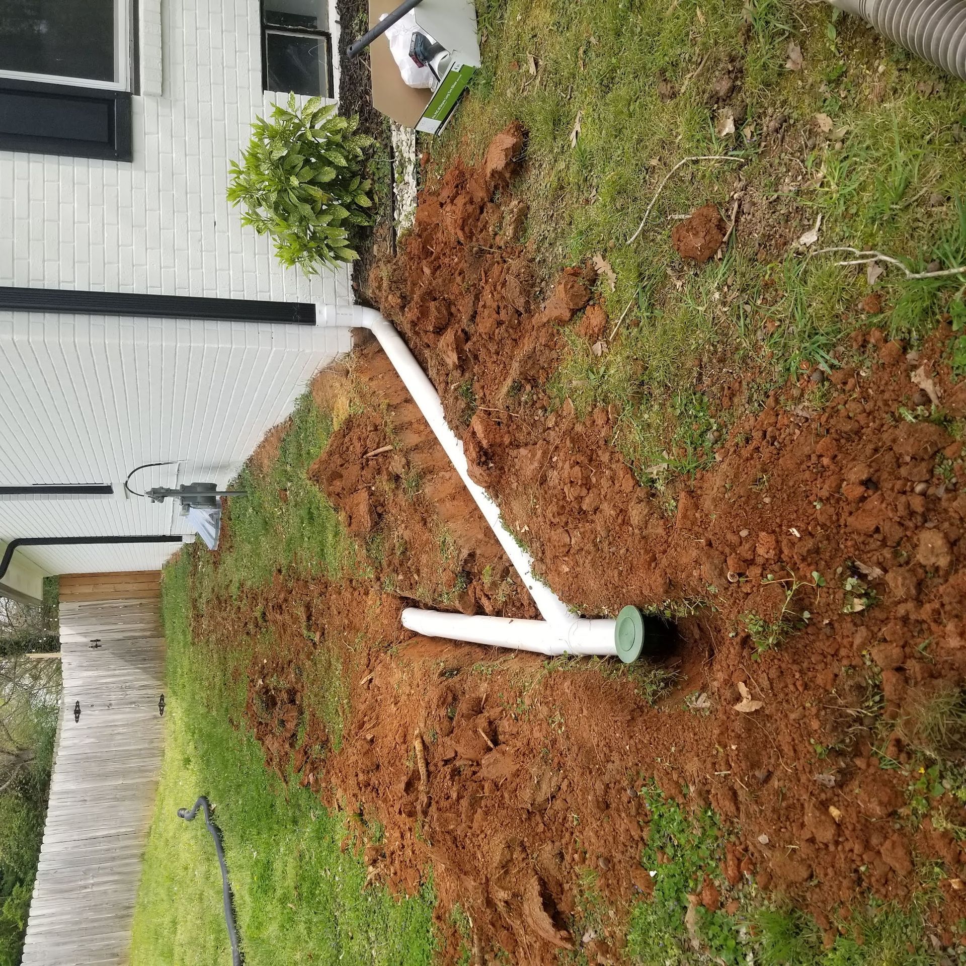 White PVC pipes installed in a trench on a grassy lawn next to a house. Dirt surrounds the pipes.