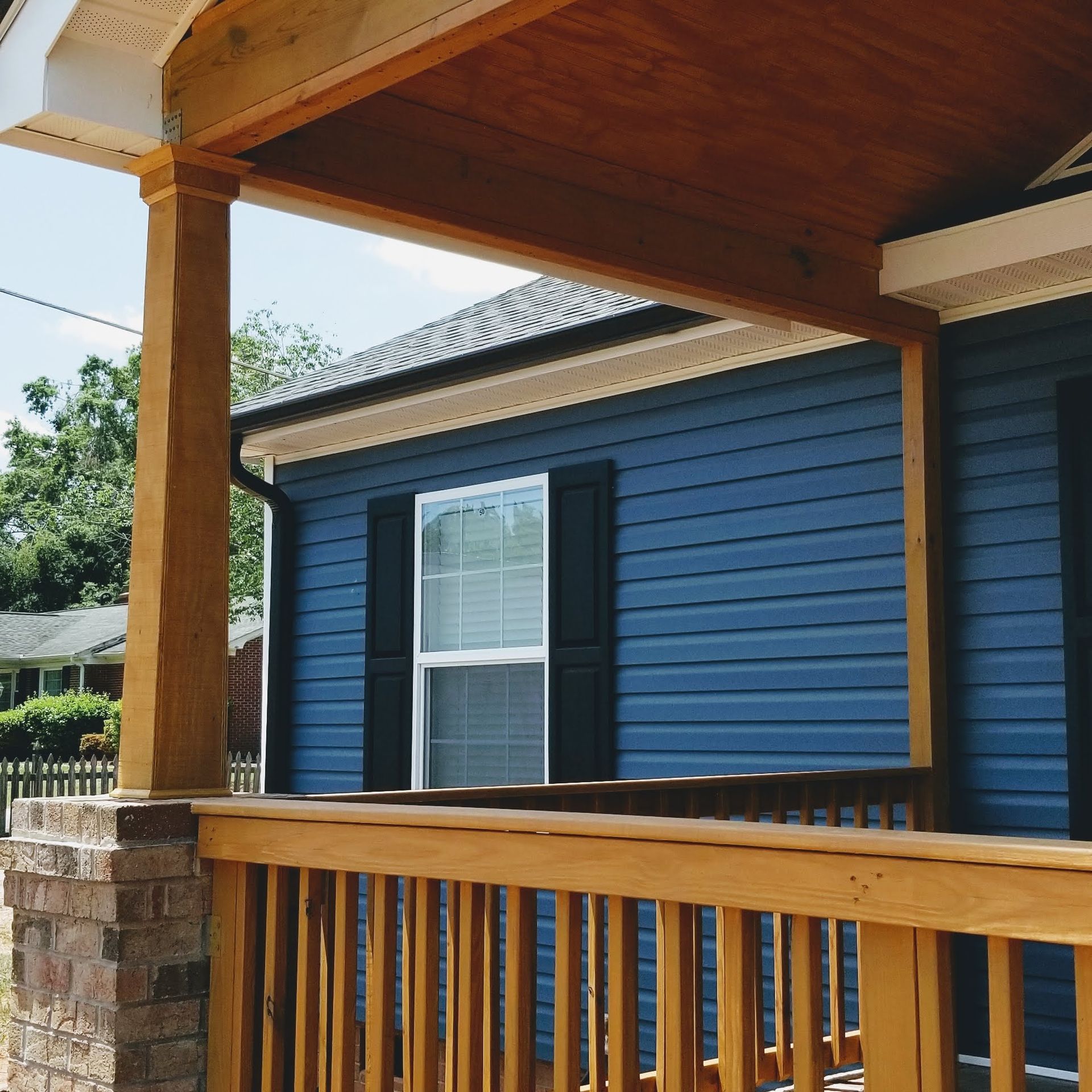 Blue house with wooden porch and railings, sunny day.