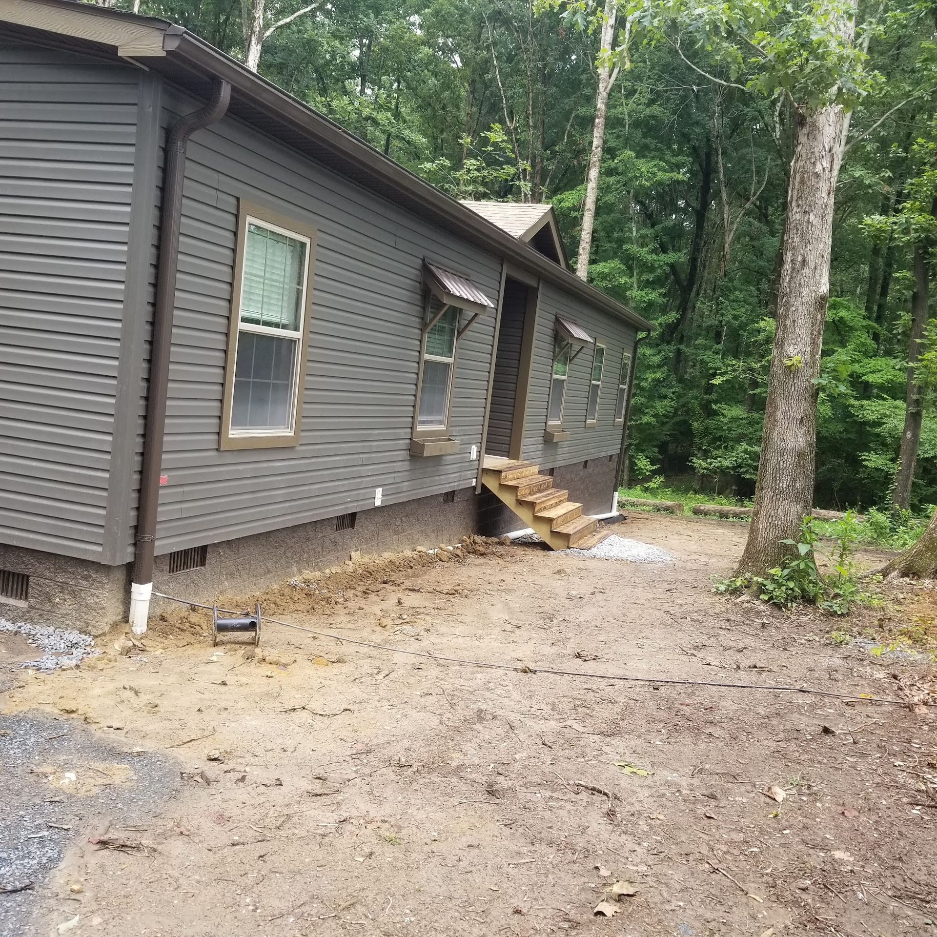 Gray cabin with small wooden steps, surrounded by dirt and trees.