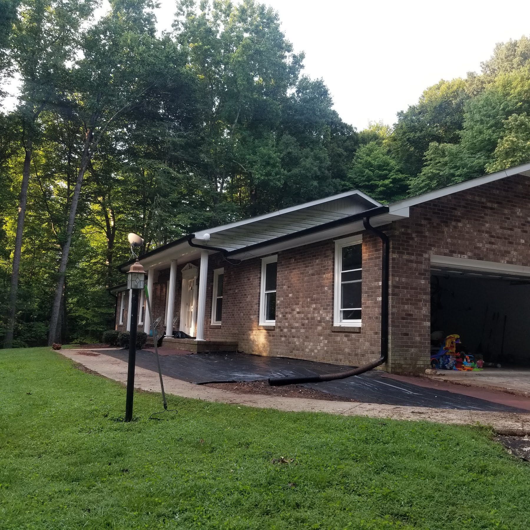 Brick house with white trim, black gutters, and a garage in a wooded setting.