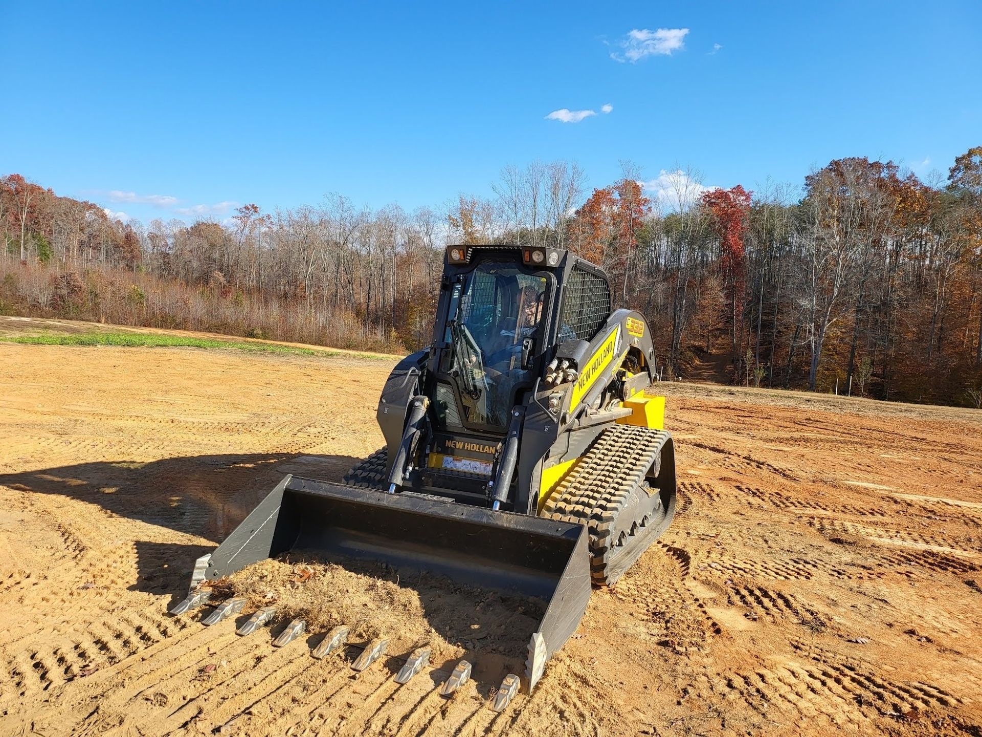 Yellow and black skid steer loader on a construction site under a blue sky.