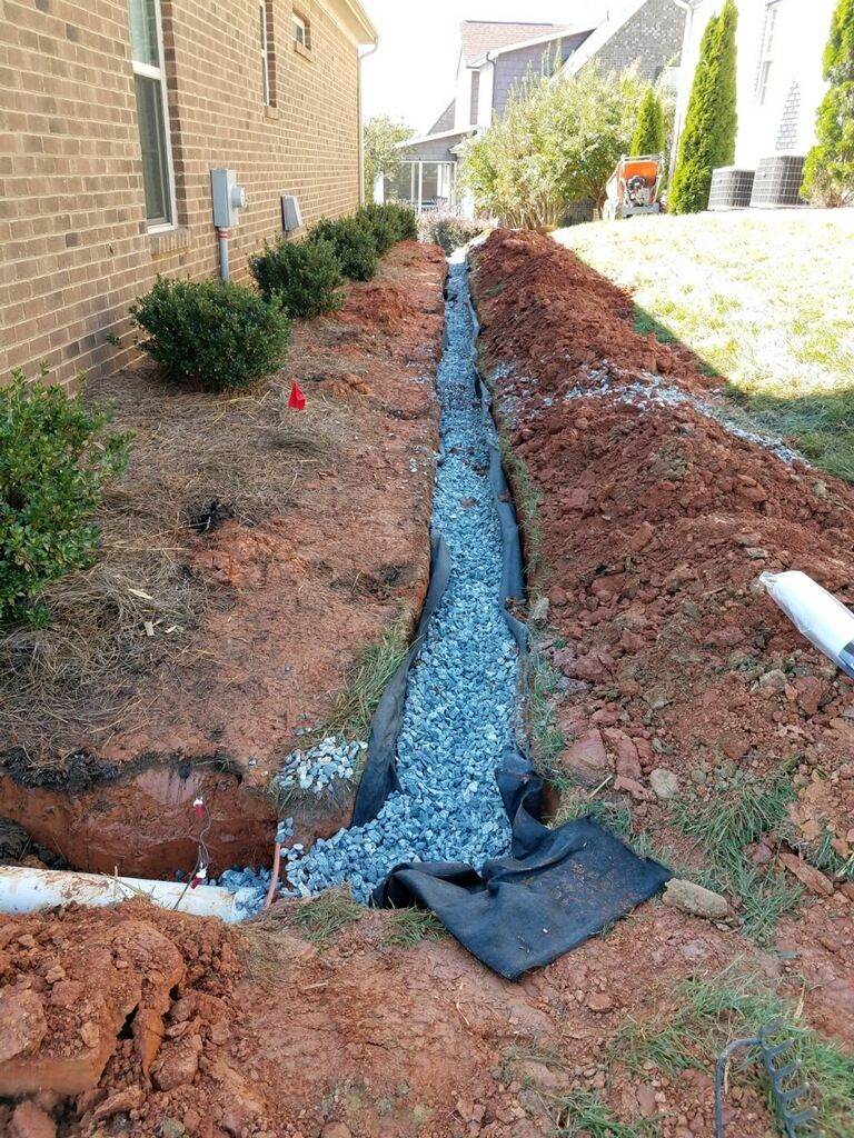 A trench with gravel and landscaping fabric for drainage next to a brick building.