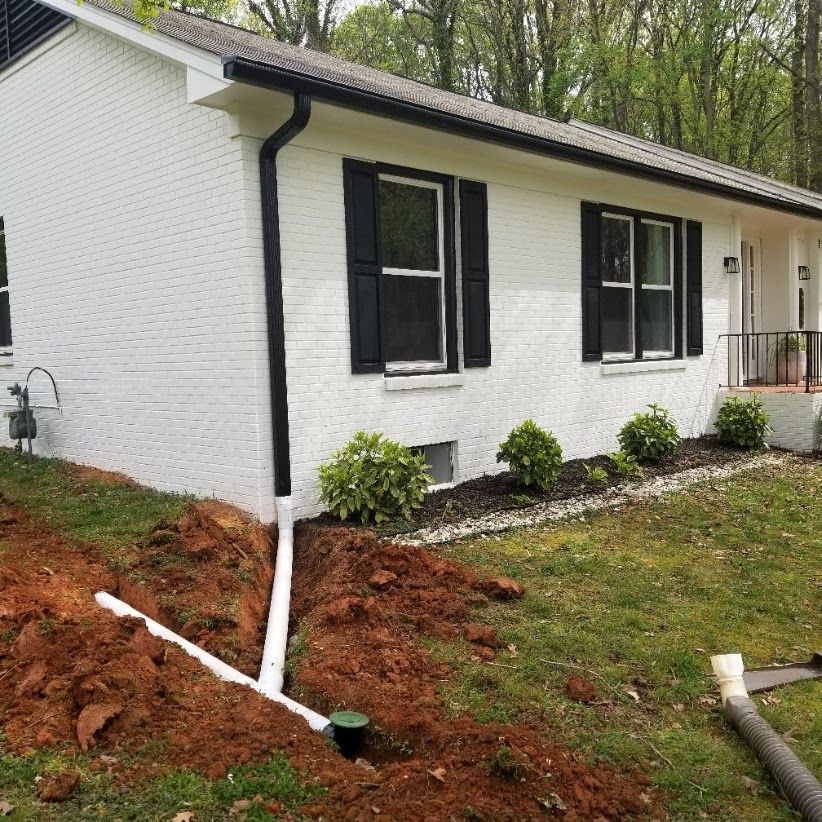 White brick house with black trim and gutters, drainage pipes in a dirt trench on the lawn.