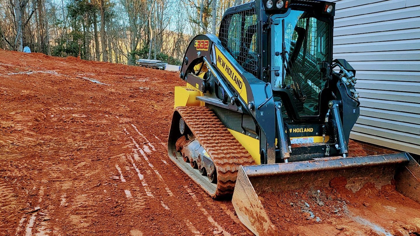 New Holland skid steer loader grading red soil on a construction site.