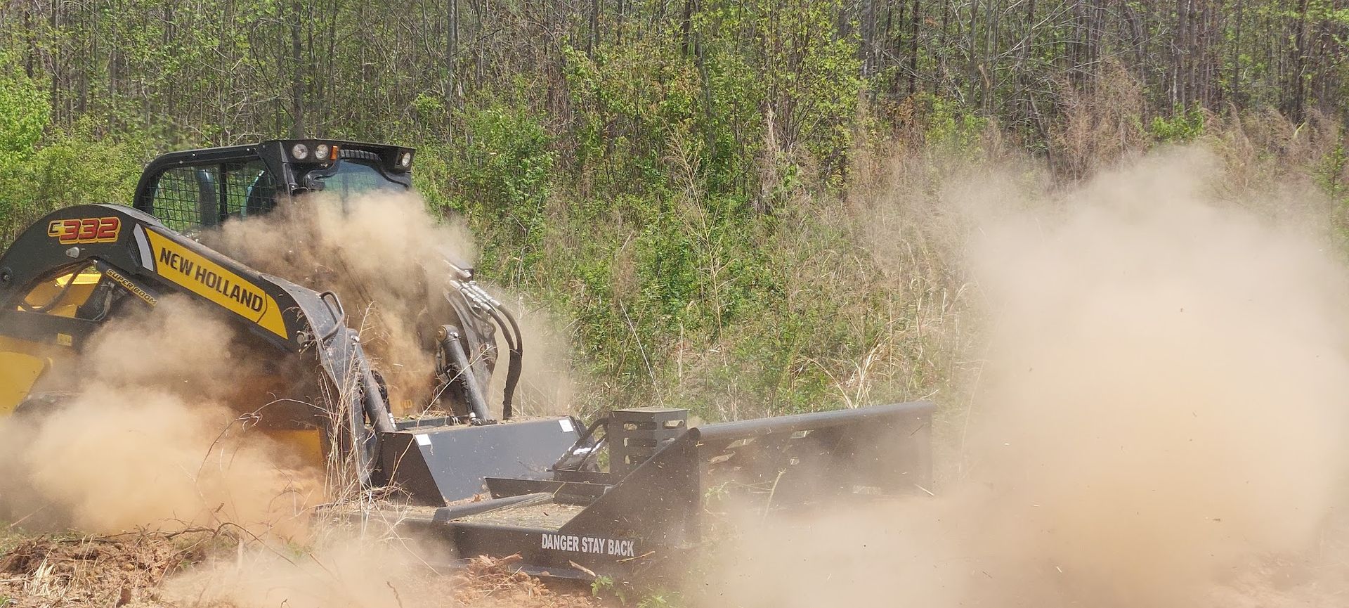 A skid steer mulcher kicking up a cloud of dirt and debris in a field.