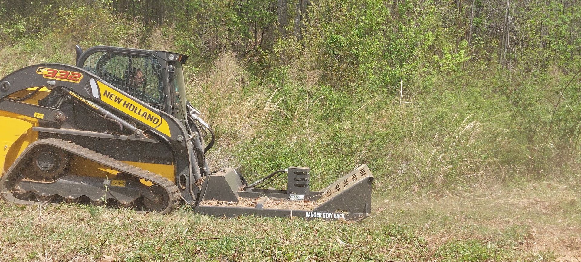 Yellow track skid steer mulching tall grass in a field.