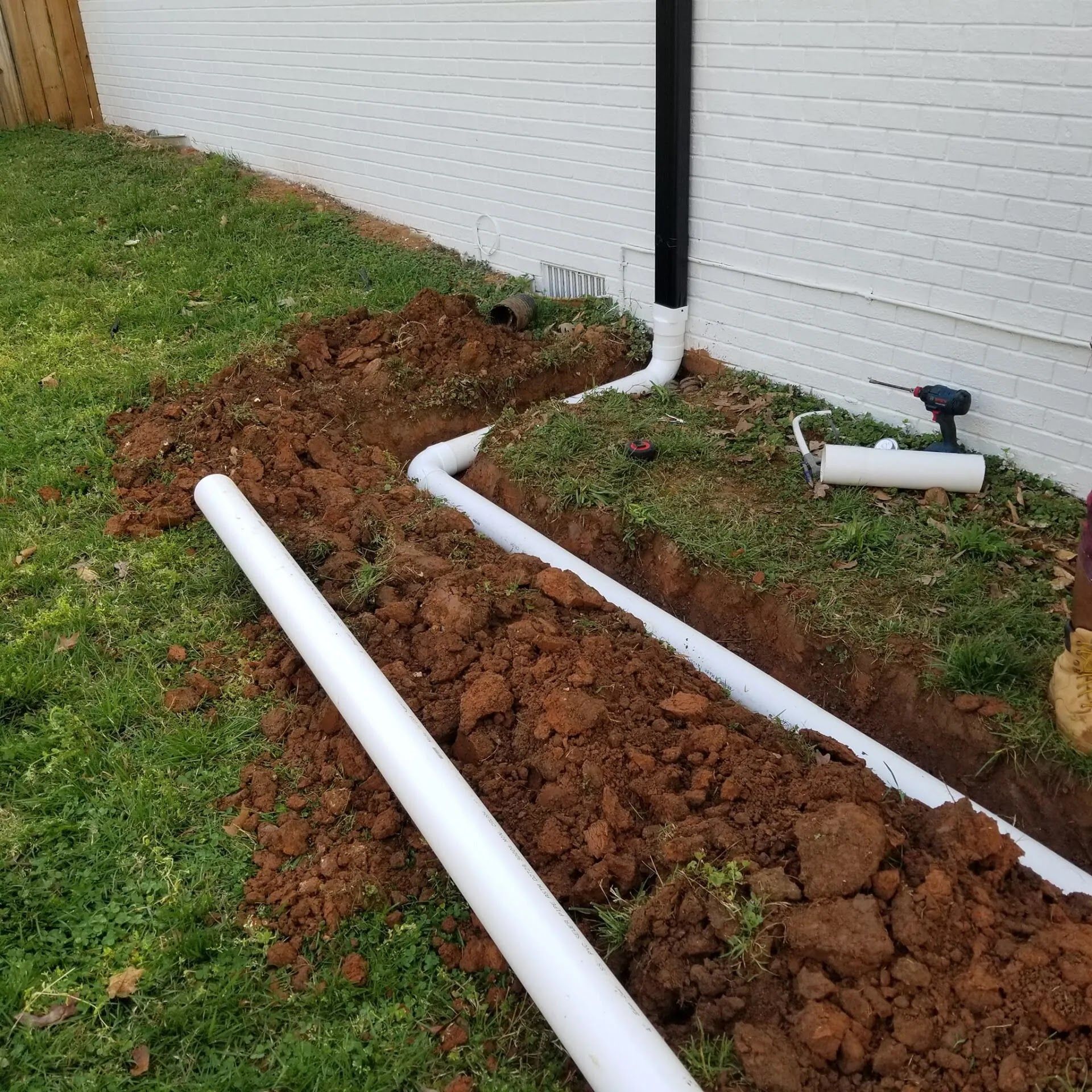 White PVC pipes in a trench near a white building, connected to a black downspout.