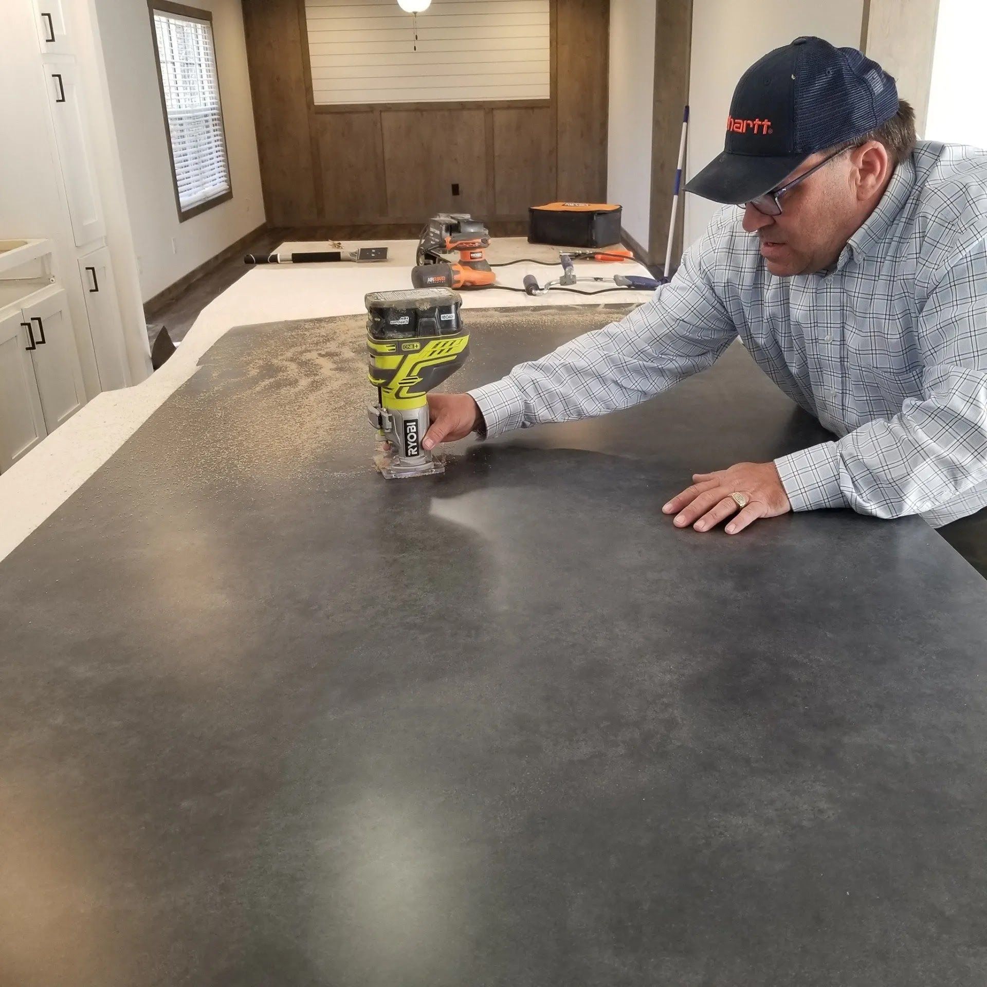 Man using a power tool on a large, gray countertop in a room.