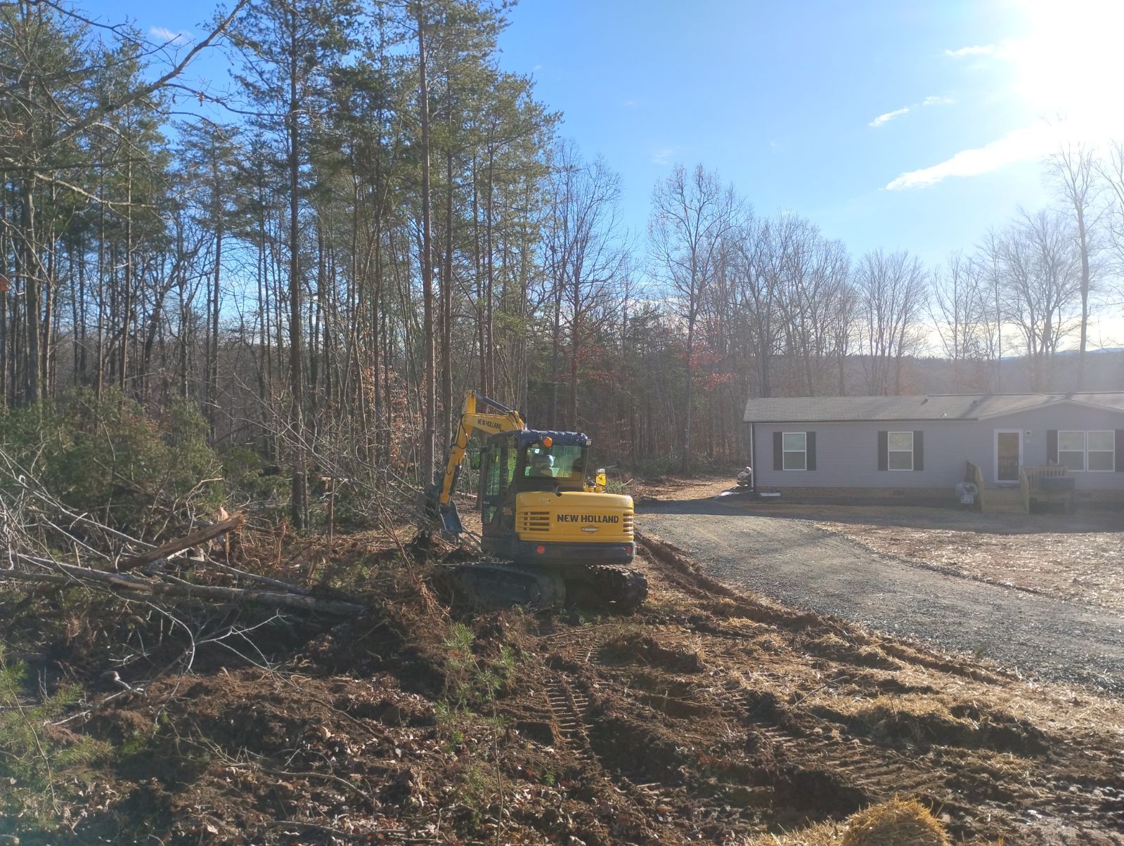 Excavator clearing brush near a residential property on a sunny day.