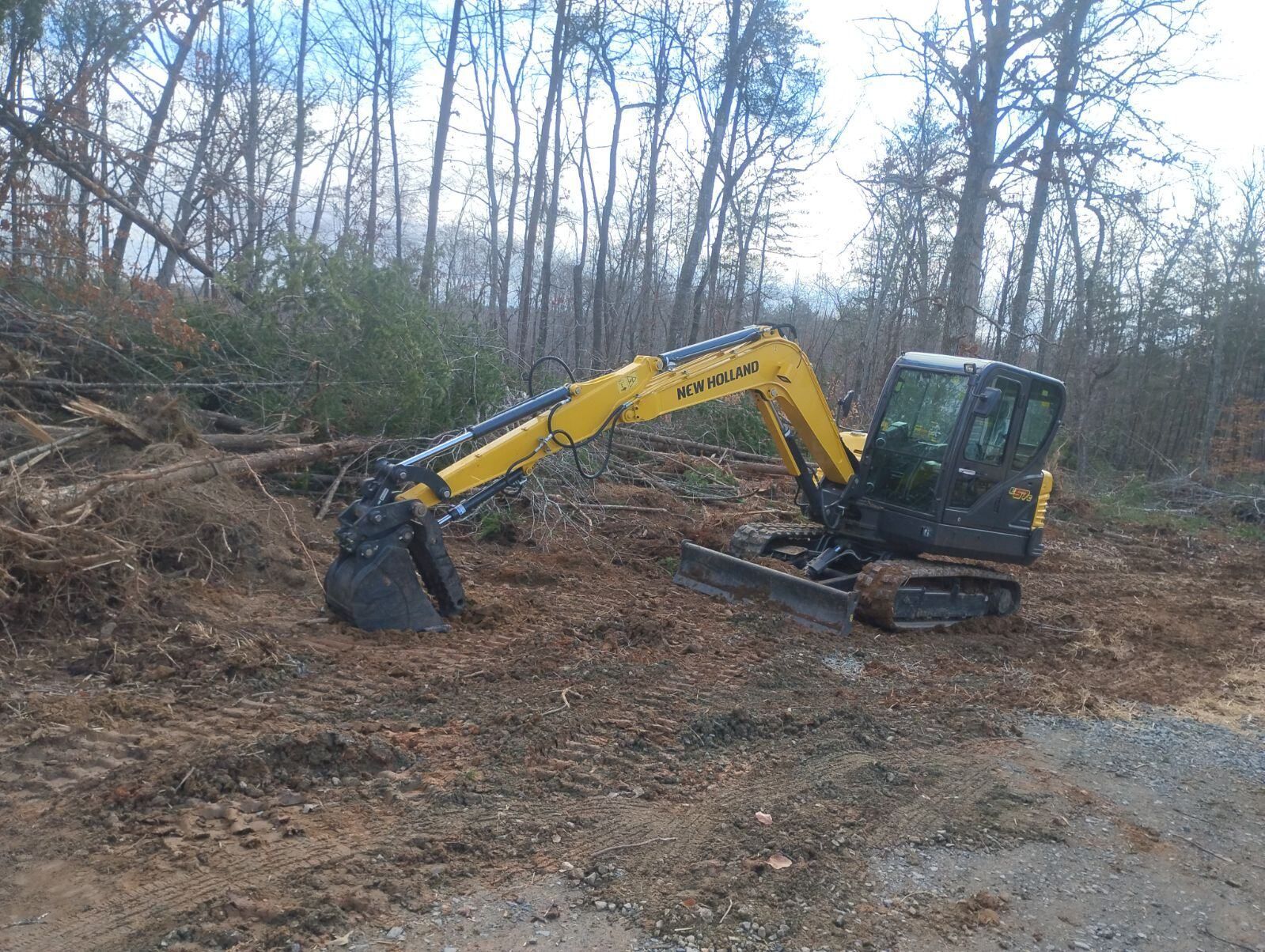Yellow excavator digging in a dirt area, with a forest background.