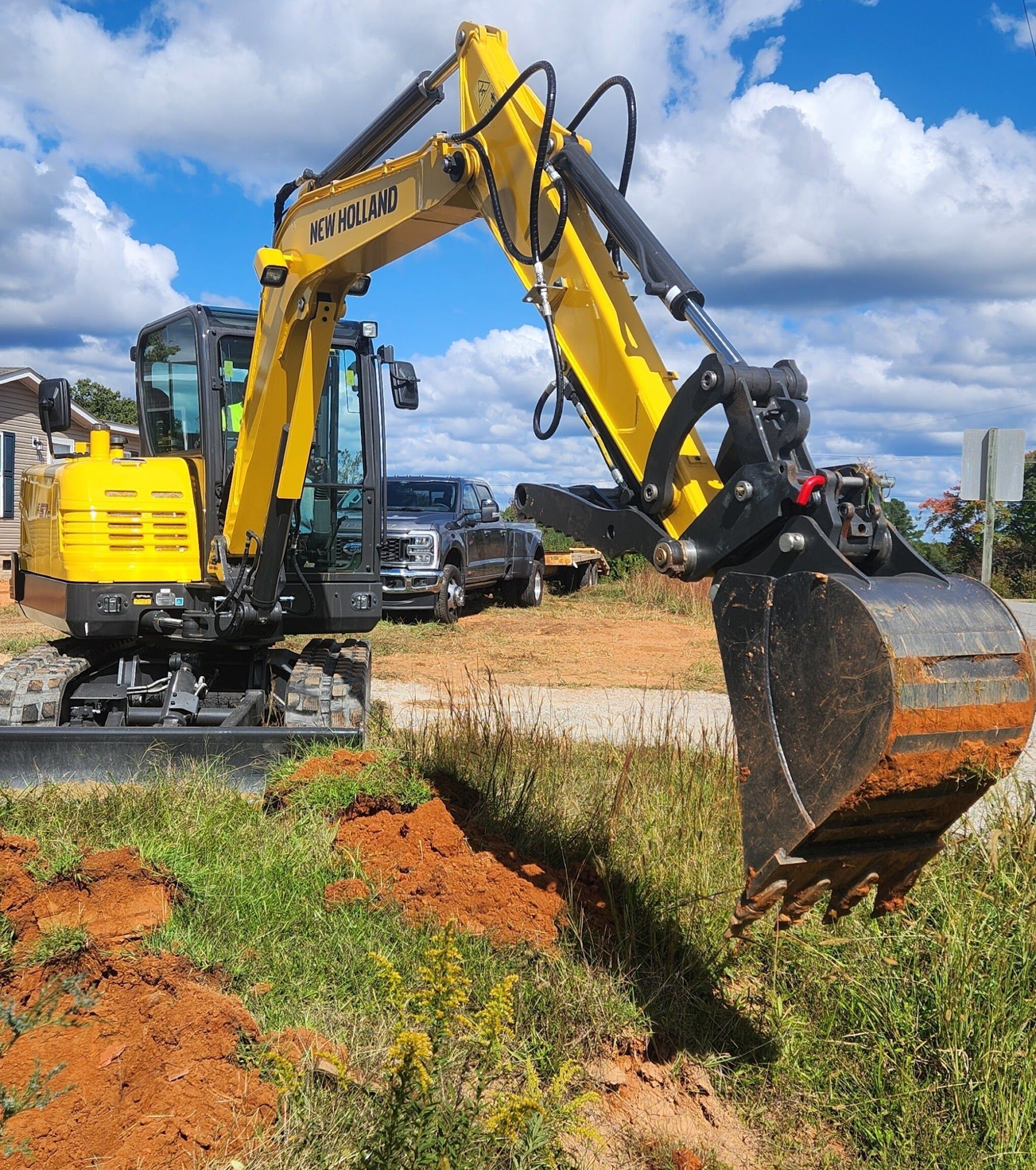 Yellow excavator digging in a grassy area with a blue sky in the background.