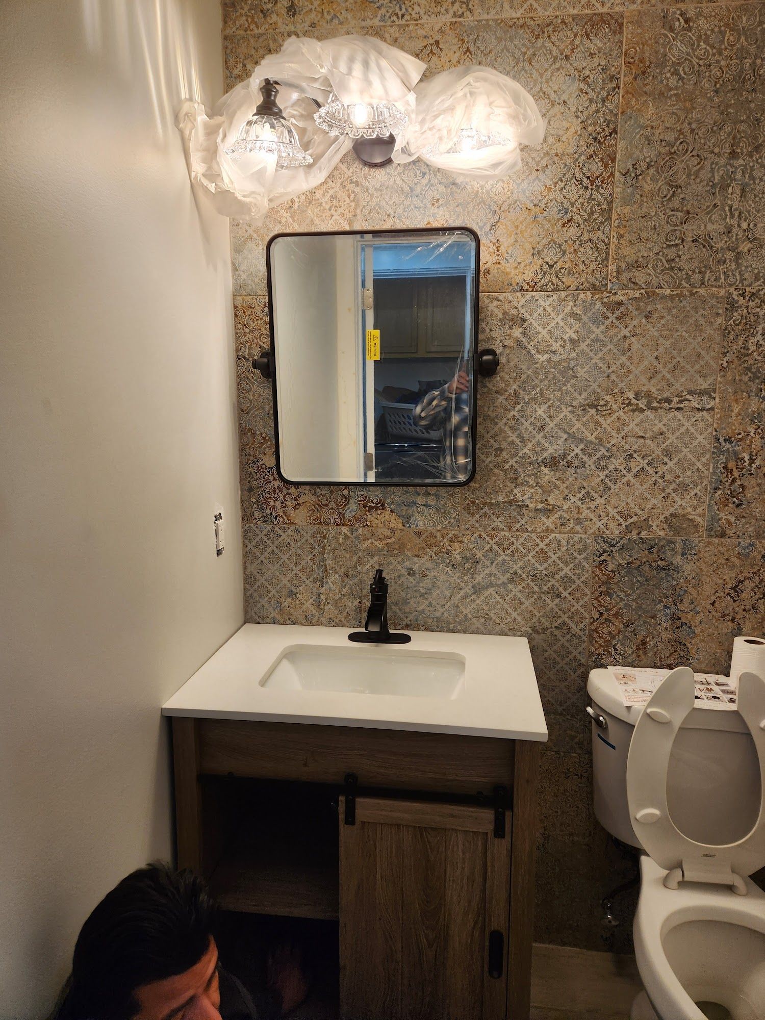 Bathroom with vanity, mirror, toilet, and decorative tiled wall. A light fixture is above the mirror.