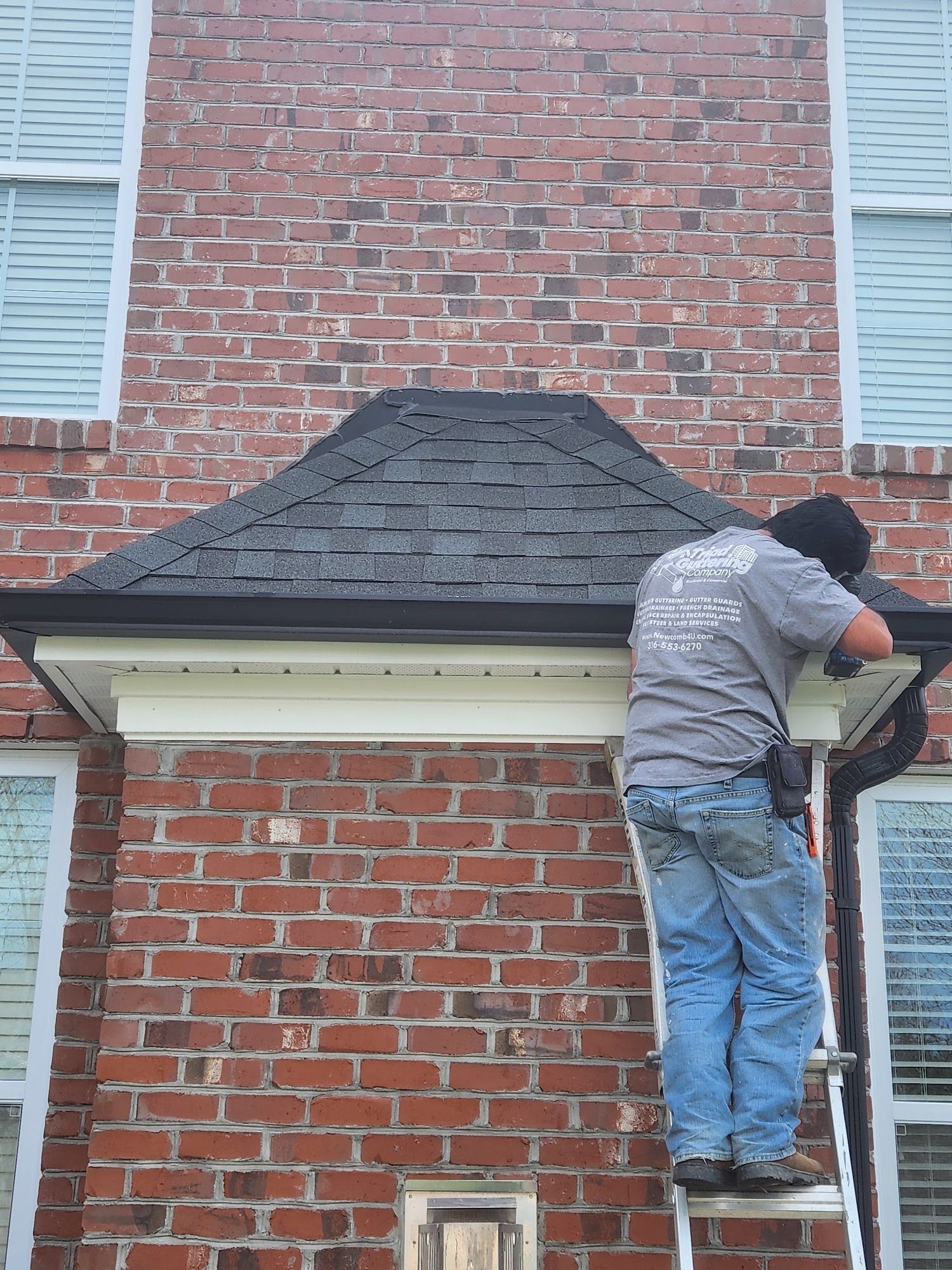 Person on ladder near brick wall, installing or repairing gutter.