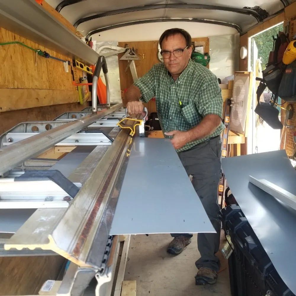 Man using a saw to cut a gray sheet of material in a workshop.