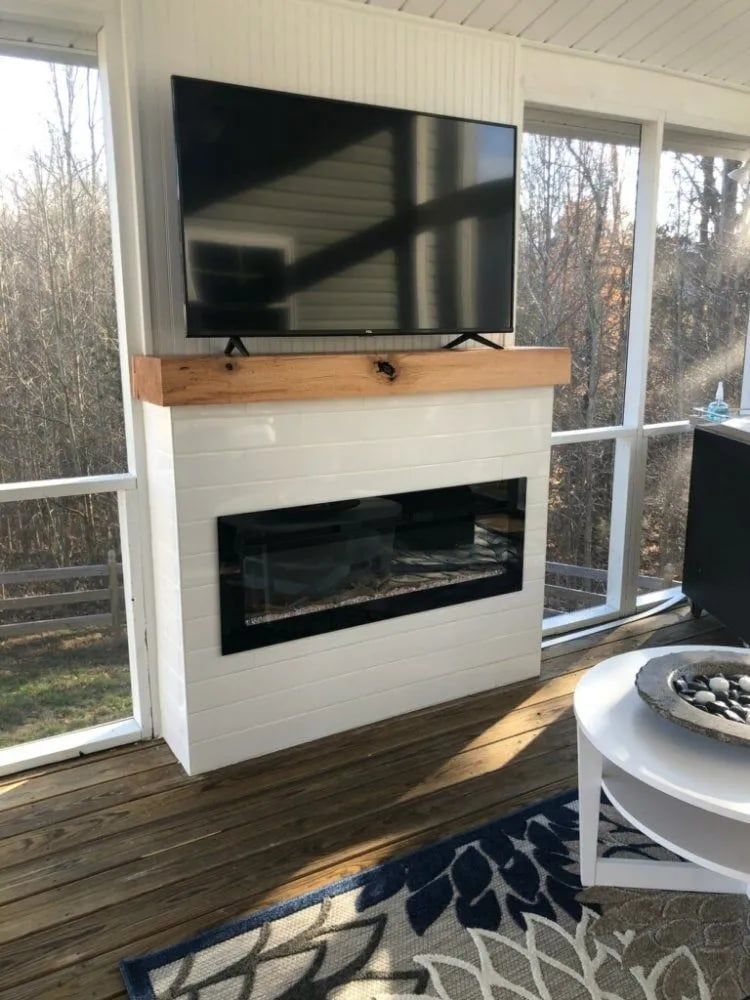 A screened-in porch with a fireplace and TV. A white cabinet encases the fireplace, topped with a wood beam.