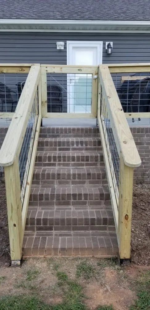 Brick stairs leading to a doorway, flanked by wooden railing with wire mesh.