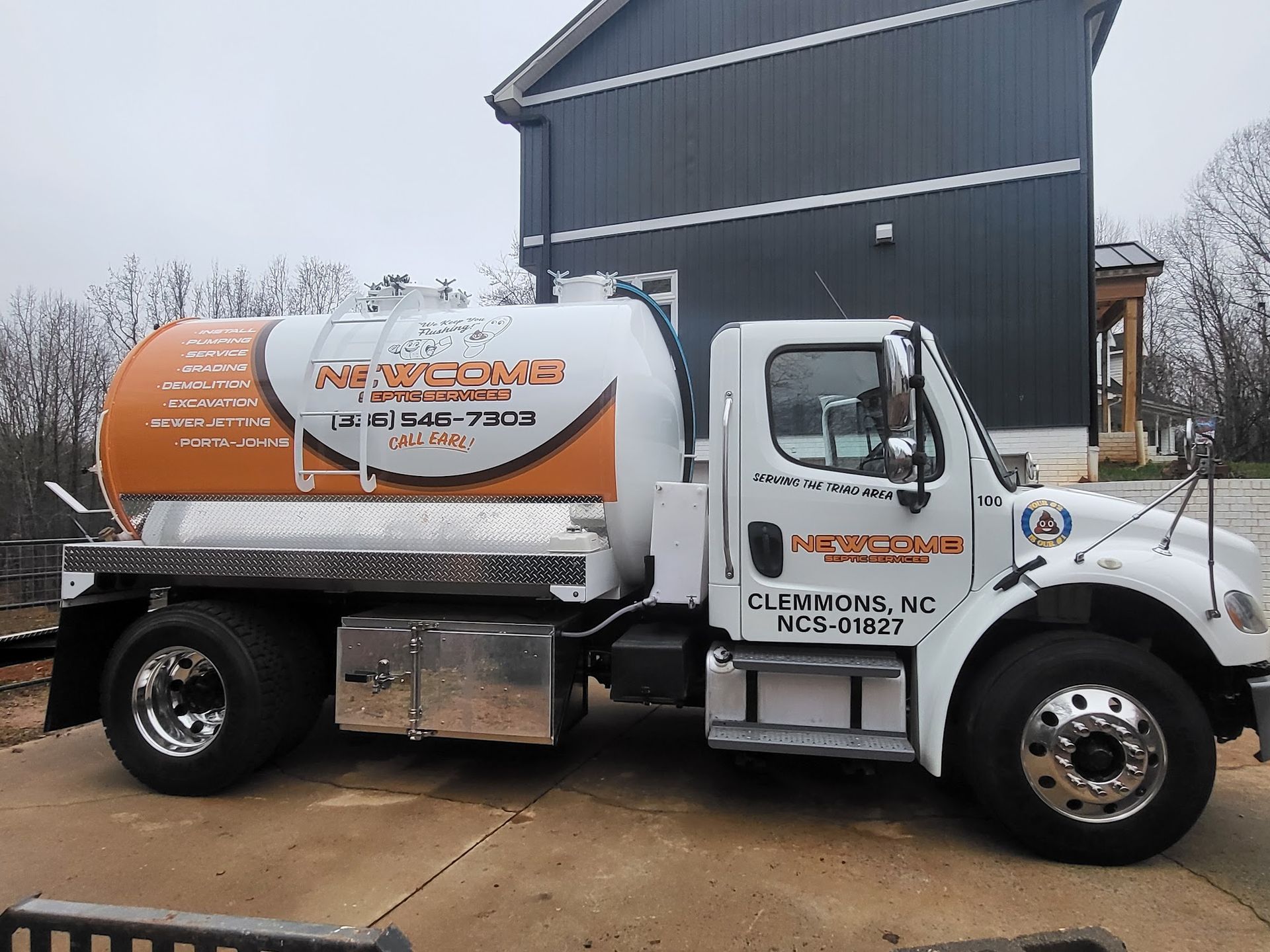 White and orange septic tank truck parked in front of a house.