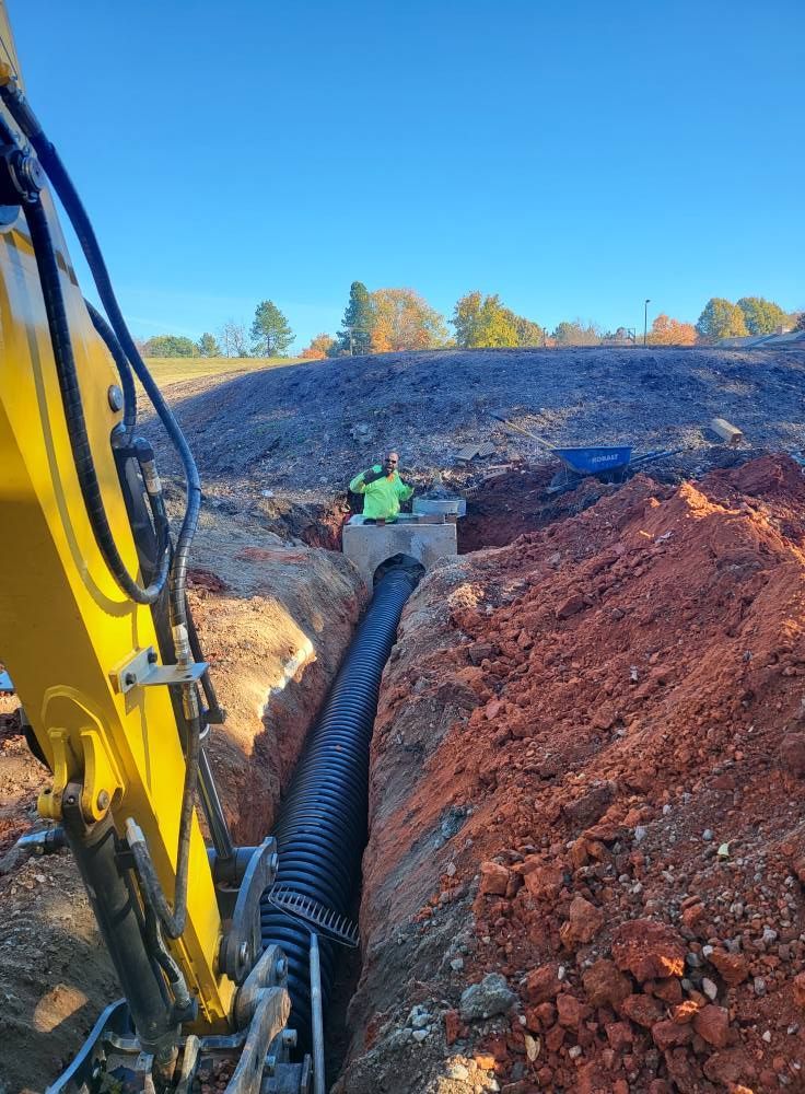 Person installing a drain pipe in a trench filled with red soil. Garden setting.