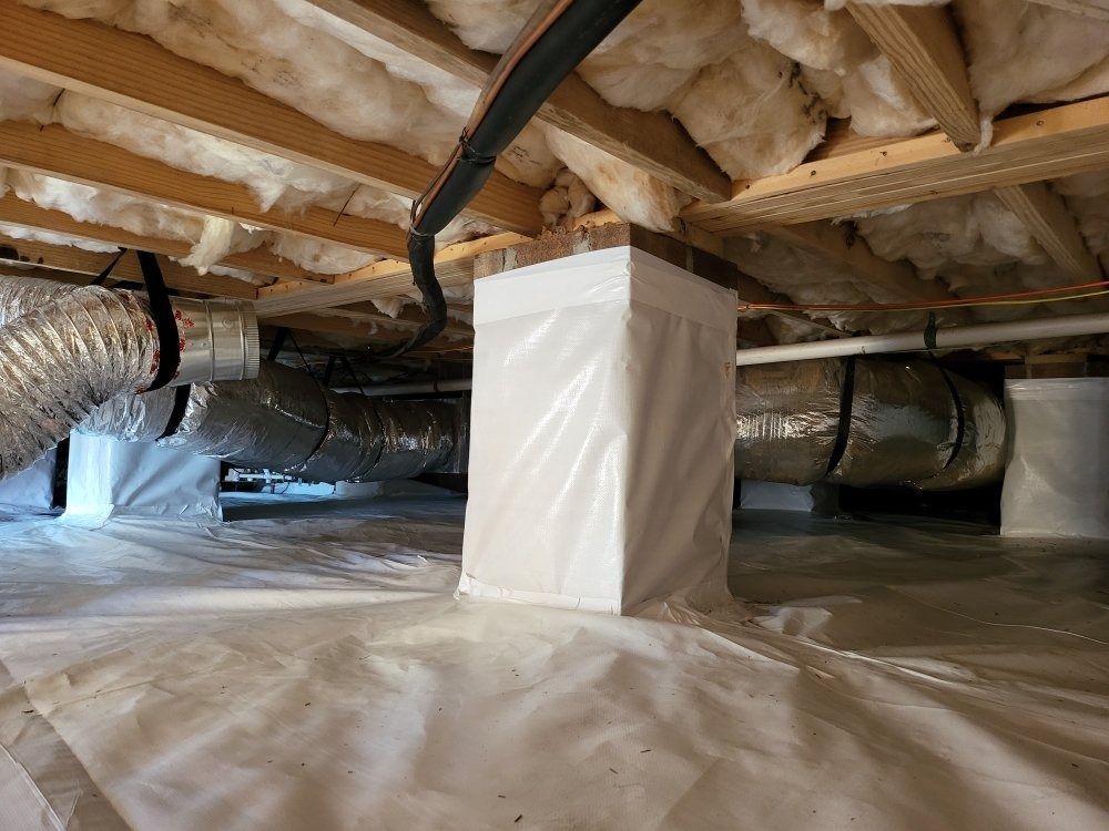 Interior view of a crawl space with white vapor barrier flooring and walls, insulation, and ductwork.