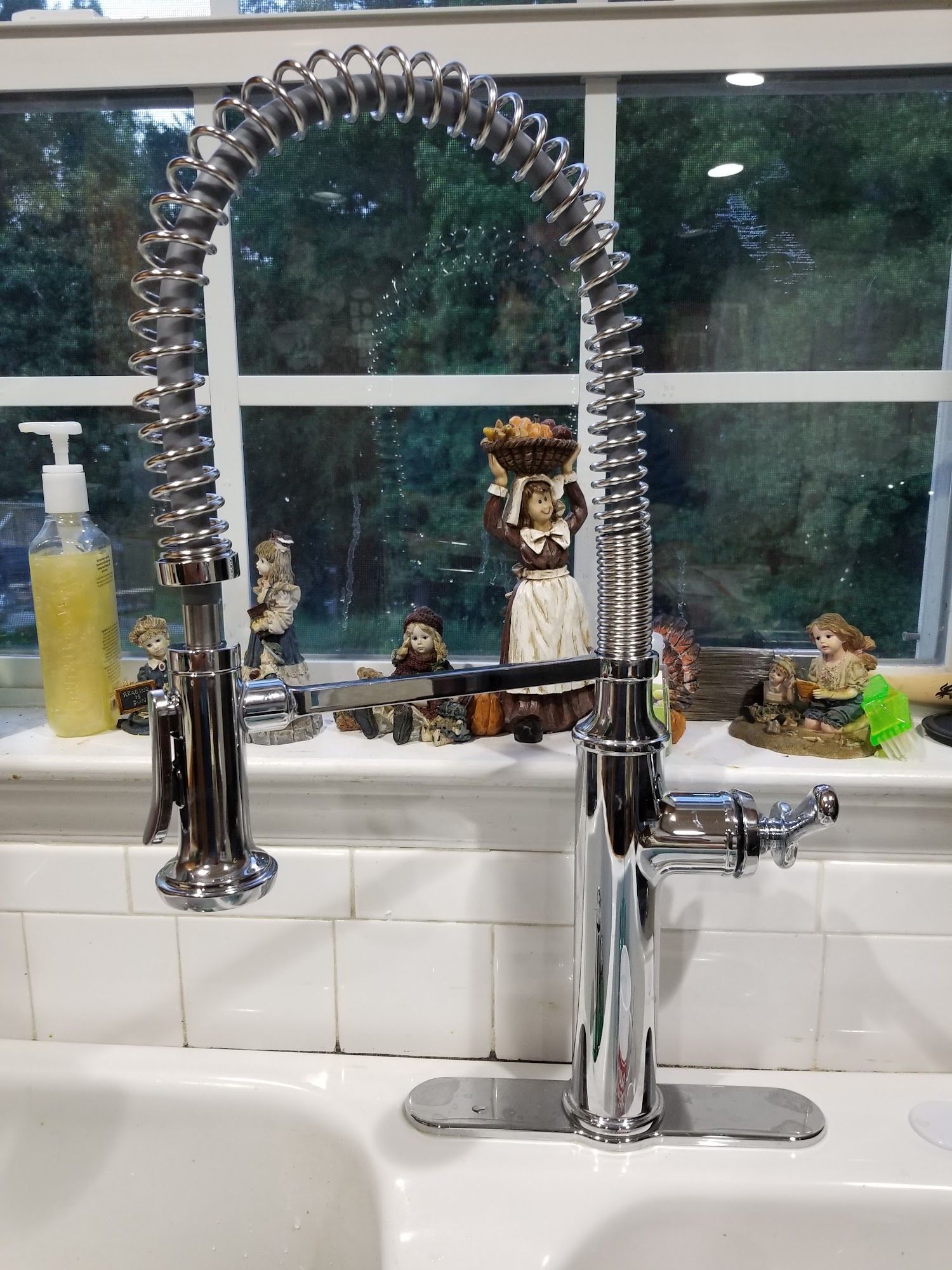Chrome kitchen faucet with coiled sprayer, mounted on a white tile backsplash.