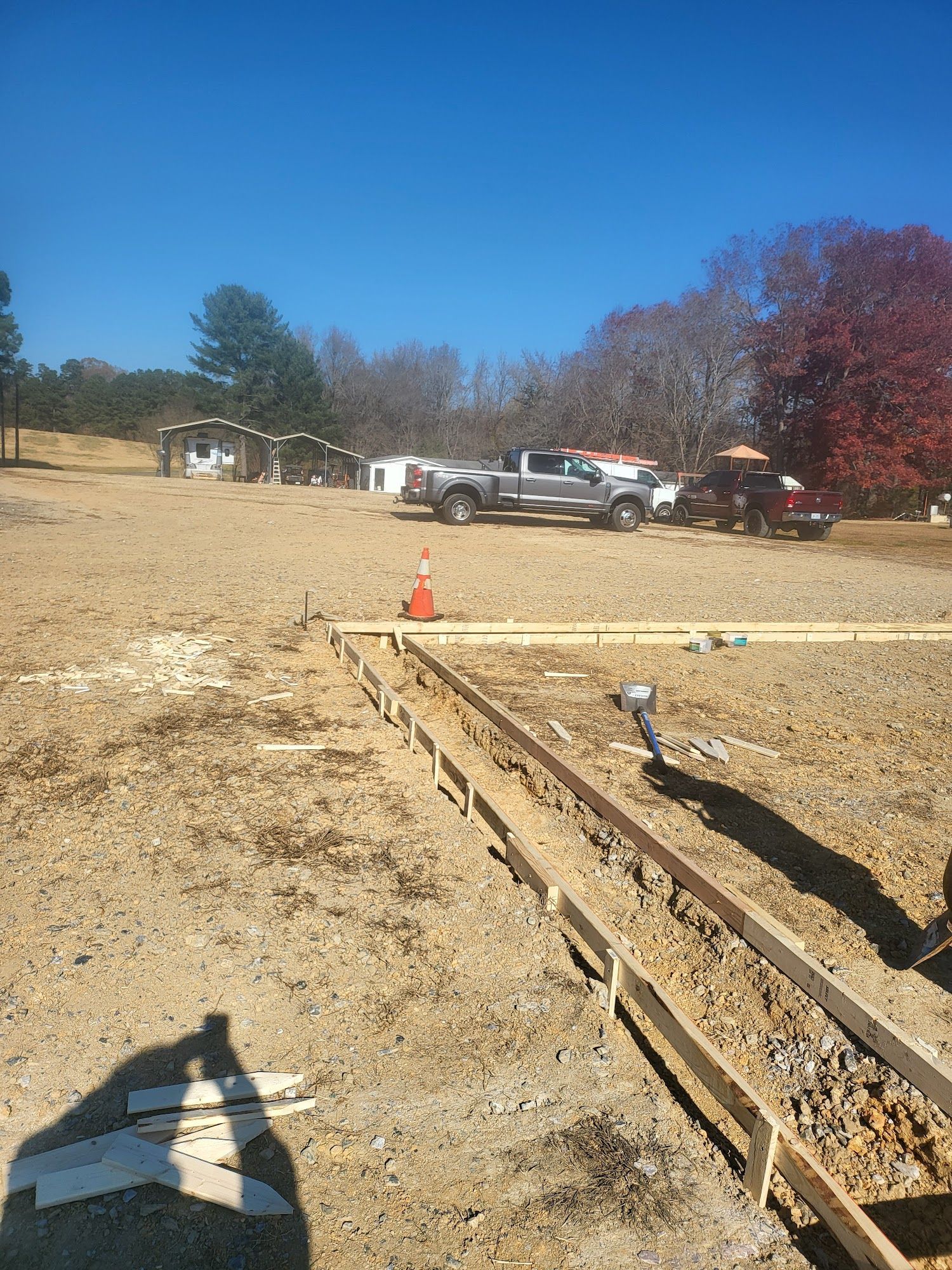Construction site with concrete forms, truck, and an orange cone under a blue sky.