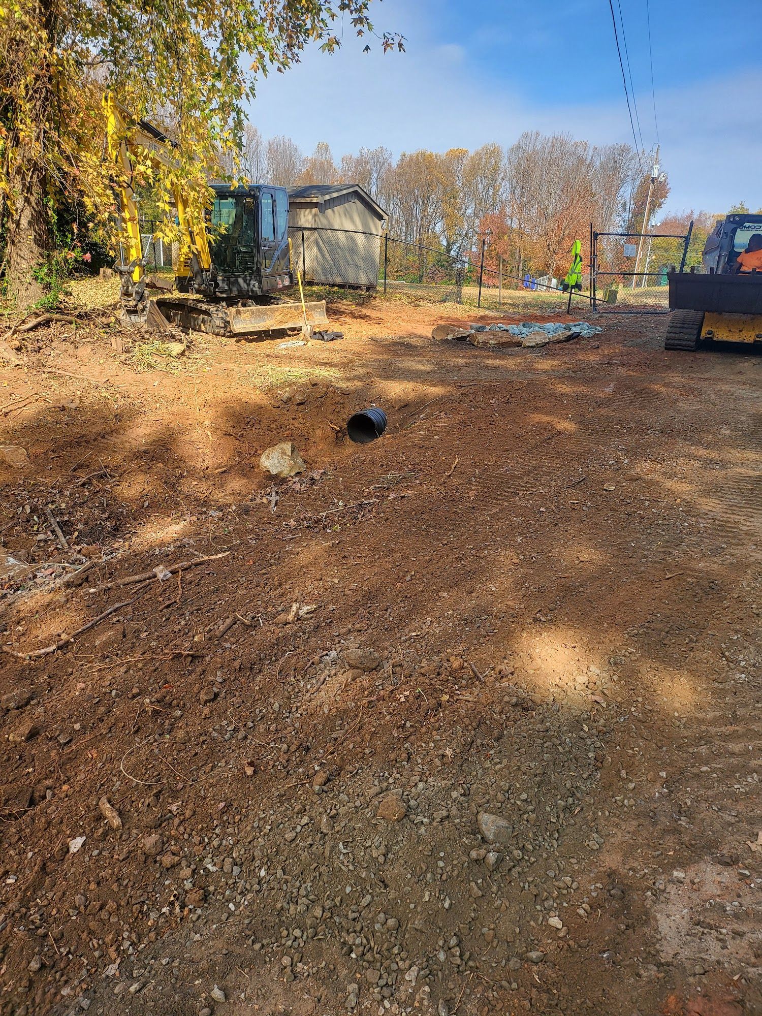 Cleared lot with dirt and gravel, small sheds, and construction equipment under a blue sky.