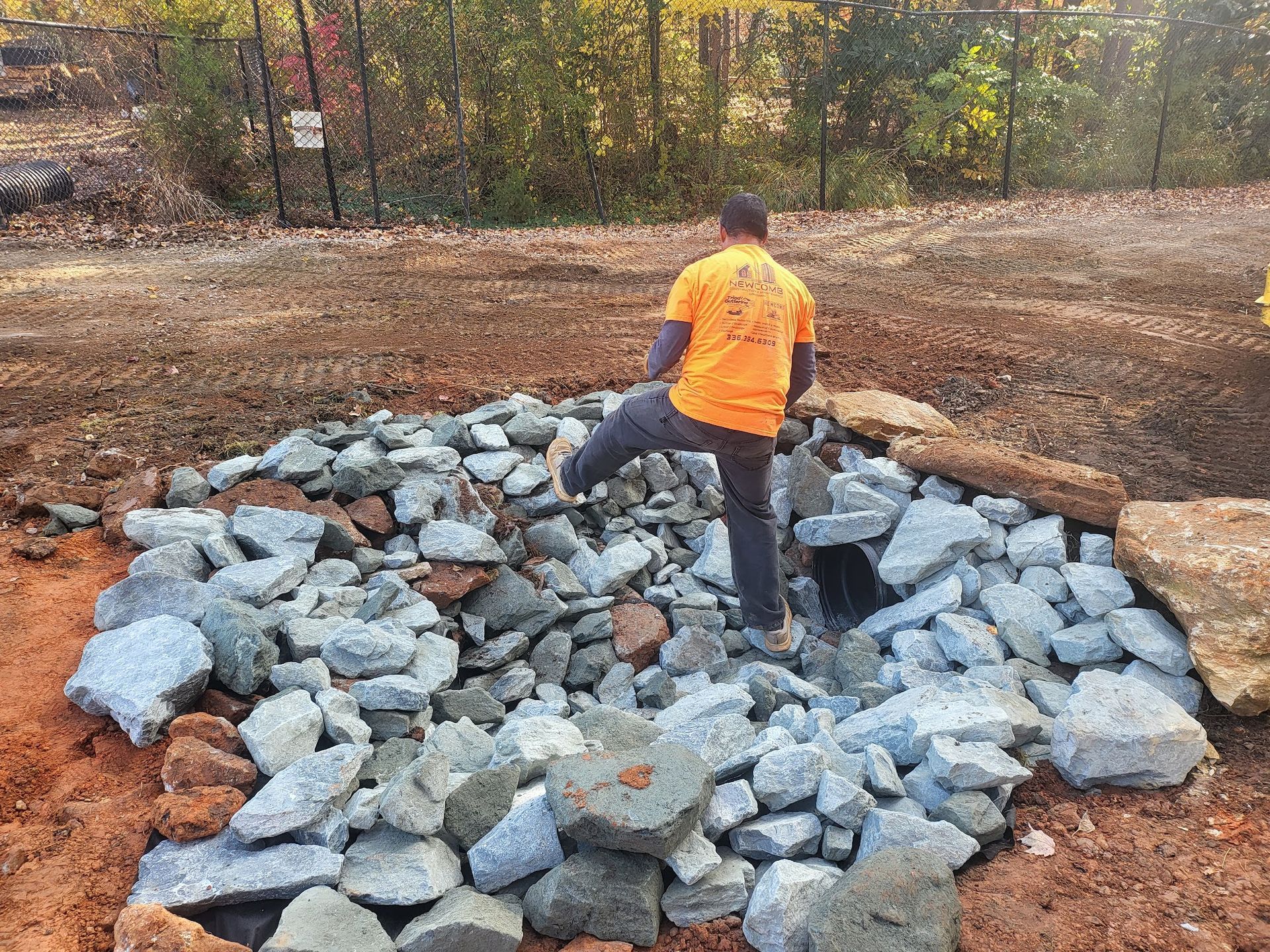 Man in orange shirt standing on rocks in a construction site.