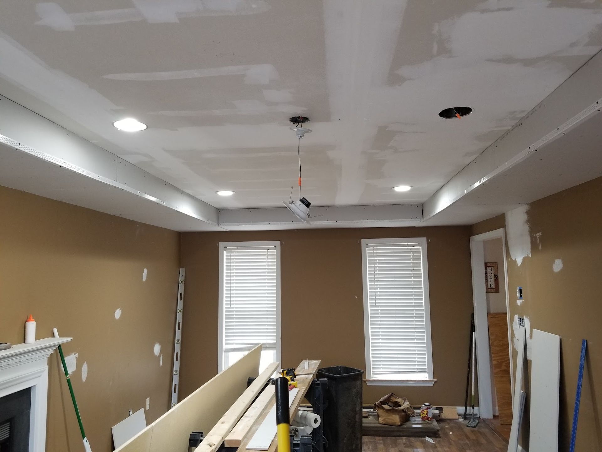 Room under construction with tan walls, white ceiling trim, recessed lights, and two windows.