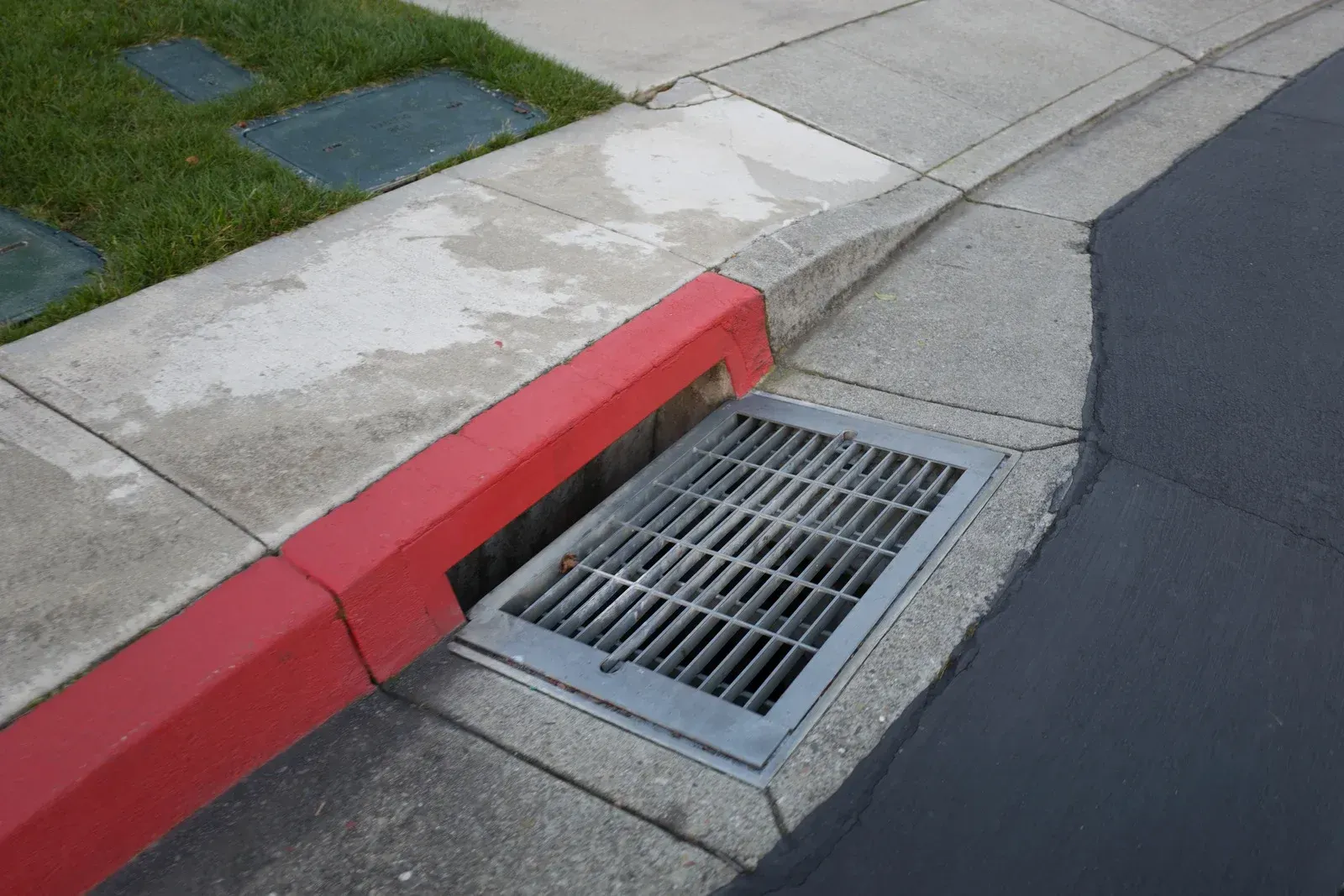 Curb with red-painted edge, metal grate storm drain, and asphalt pavement.