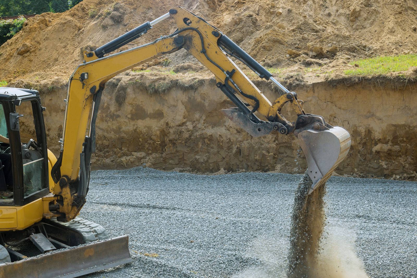 A bulldozer pouring gravel into a trench at a construction site.