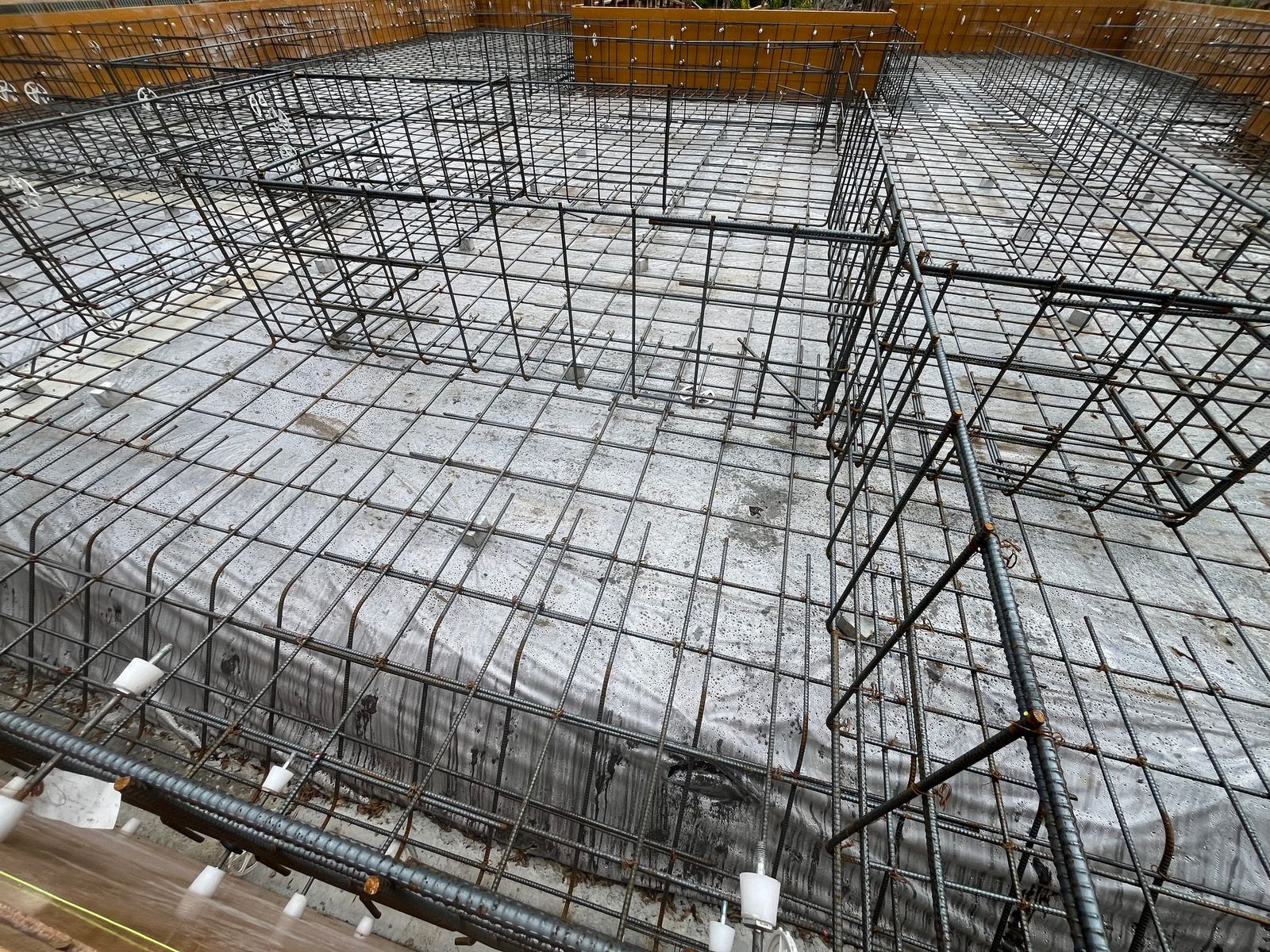 Construction site: Rebar grid laid within a rectangular foundation, prepared for concrete.