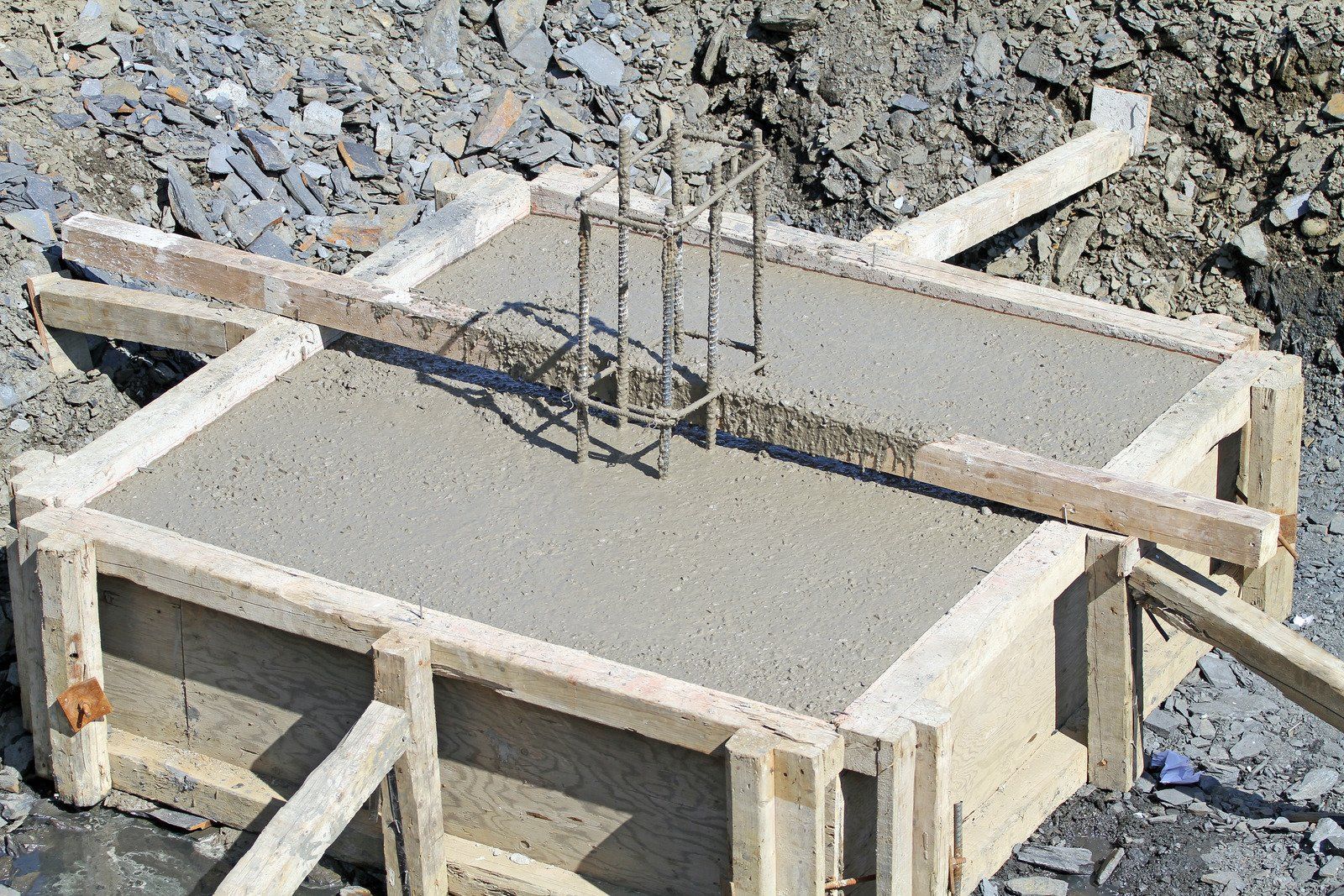 Wooden formwork holding wet concrete for a foundation, with reinforcing steel bars visible.