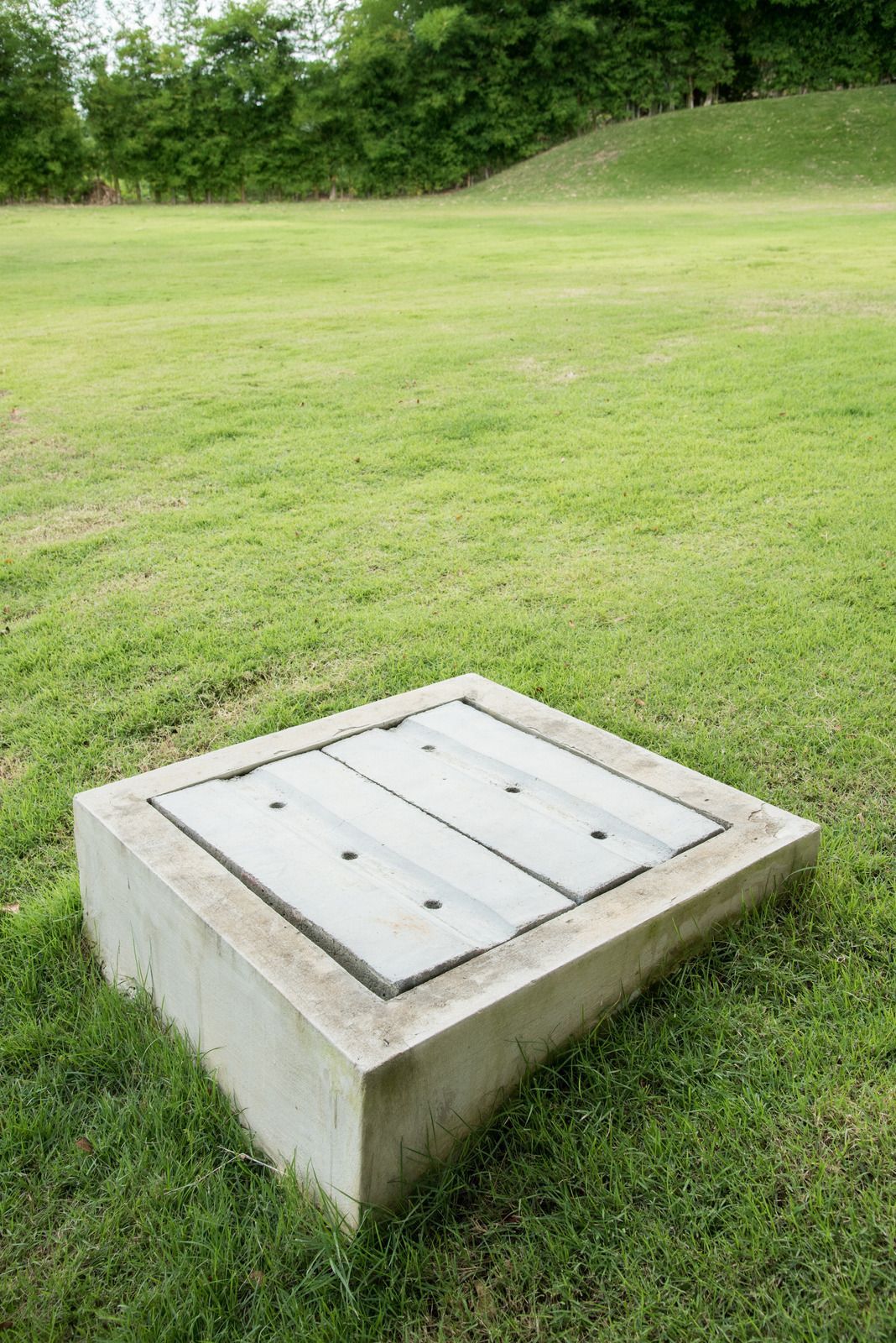 Concrete drain culvert with dark opening, in a concrete channel, with brown-orange safety fencing.
