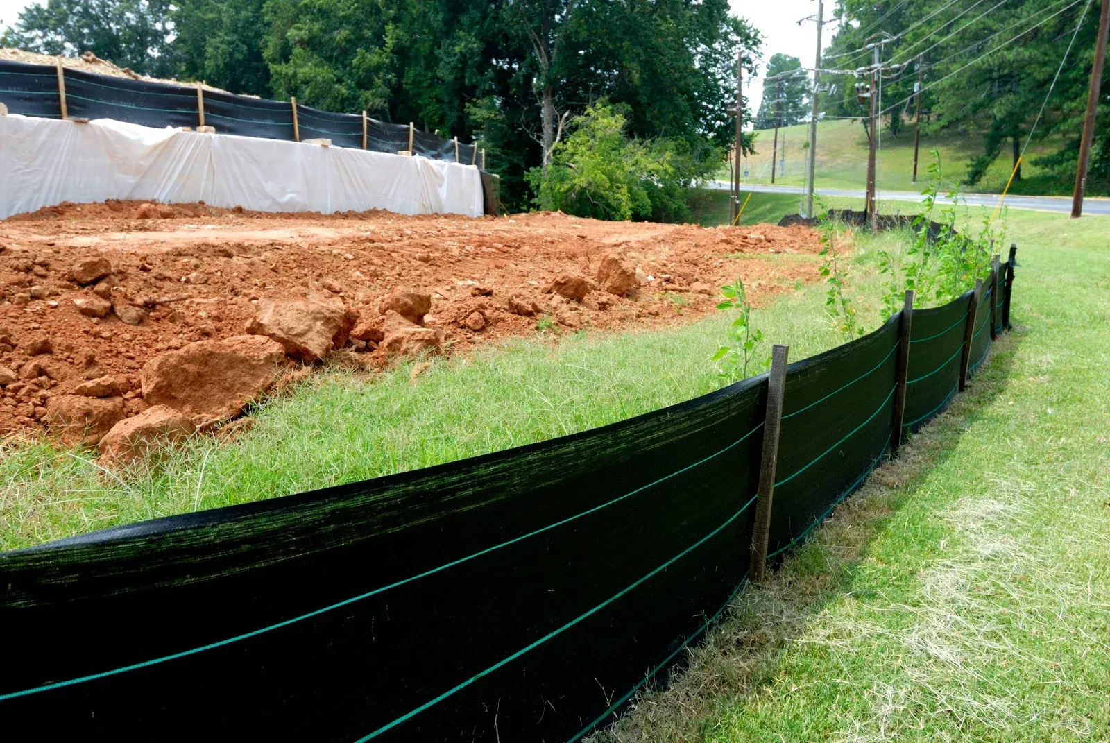Erosion control on a hillside. Brown soil spills over black grid. Green grass and a building are in the background.