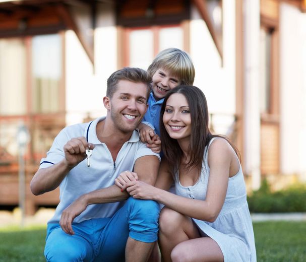 Family of three smiling, holding house keys in front of a house.